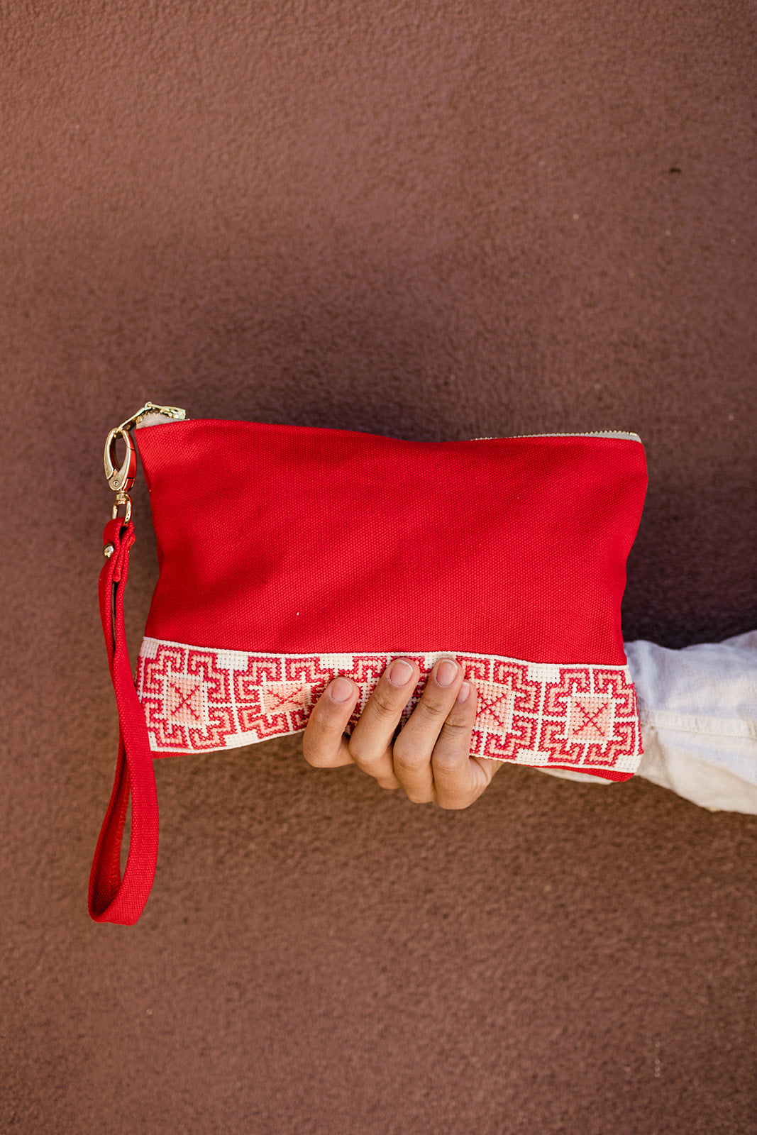 The Safa Tatreez Pouch - Red showcases exquisite Palestinian tatreez with intricate geometric patterns along the bottom edge. Hand-embroidered with care, it supports fair trade practices.