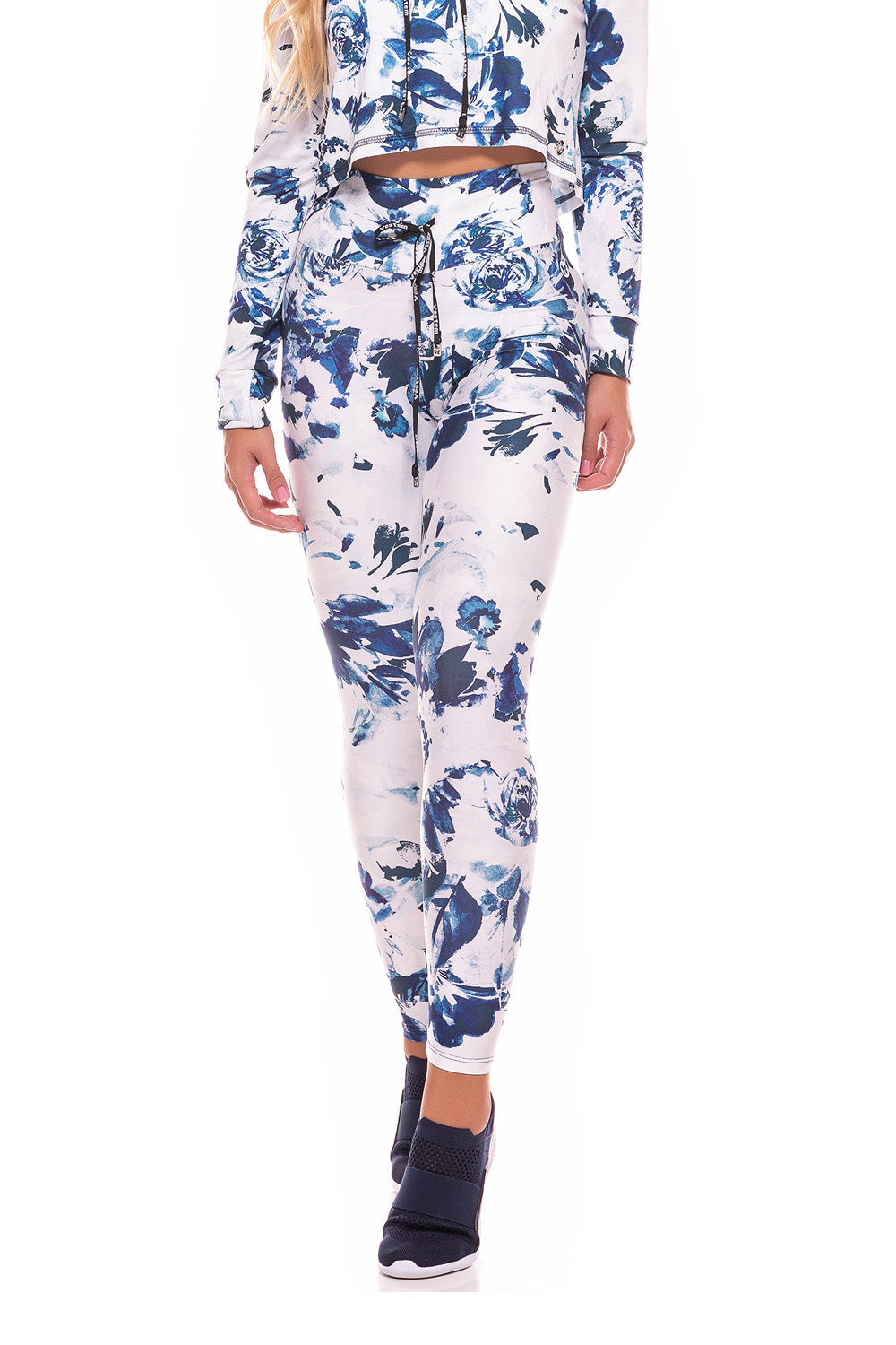 Wearing the Trust Drawstring Legging in a matching blue and white floral design with tummy control, a person poses near a white chair on a wooden floor indoors.