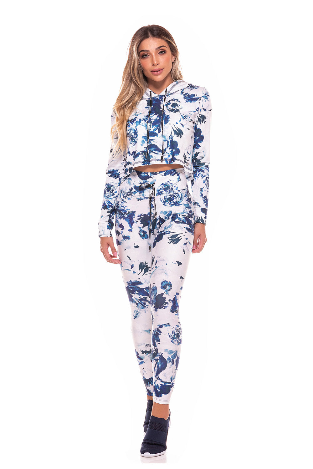 Wearing the Trust Drawstring Legging in a matching blue and white floral design with tummy control, a person poses near a white chair on a wooden floor indoors.