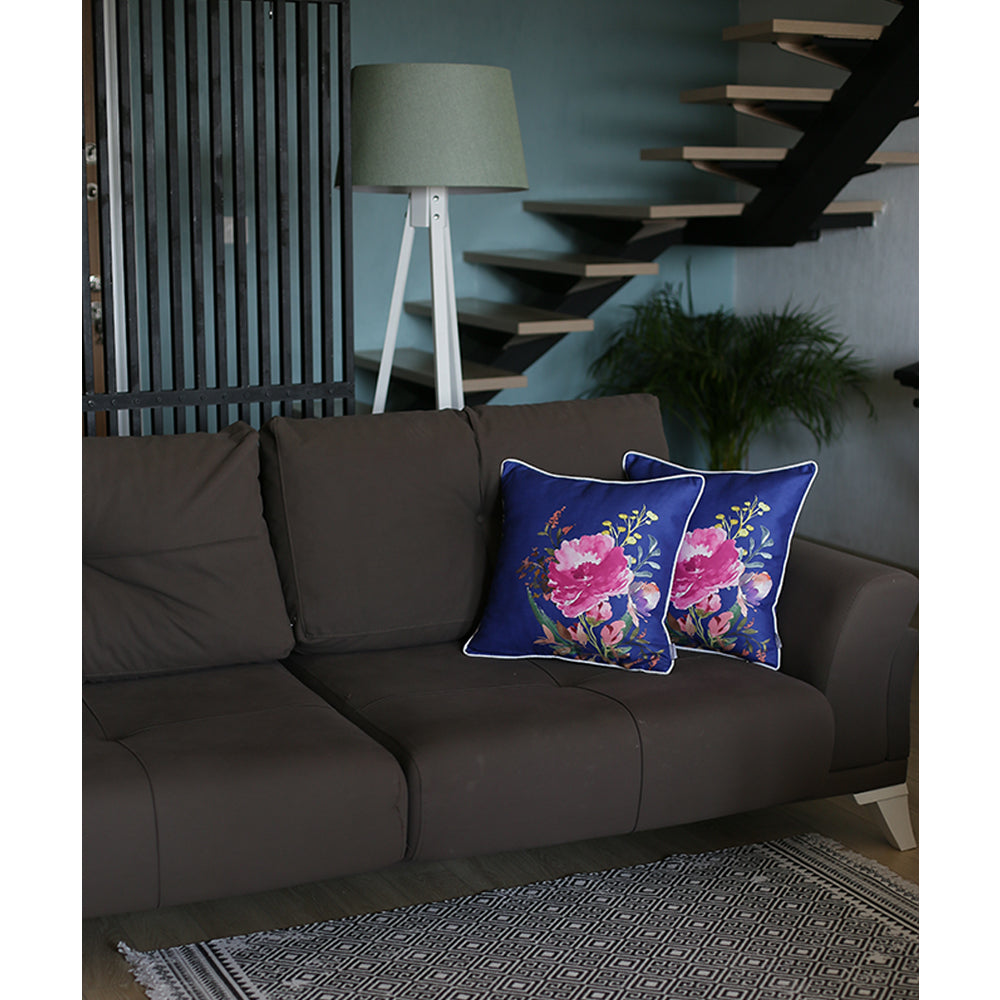 A gray sofa with two Blue Watercolor Flowers Throw Pillow Covers (18''x18", set of 2) featuring hidden zipper closures is placed beside a white lamp. A rug is on the floor, and a staircase and potted plant are visible in the background.