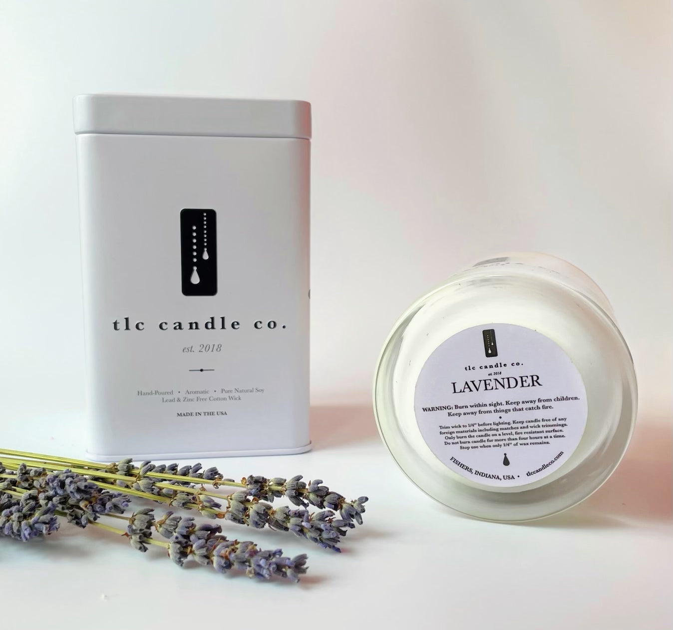 An 11 oz Lavender Soy Candle sits beside a decorative box labeled "Lavender" and a bundle of dried lavender sprigs, infused with calming essential oils.