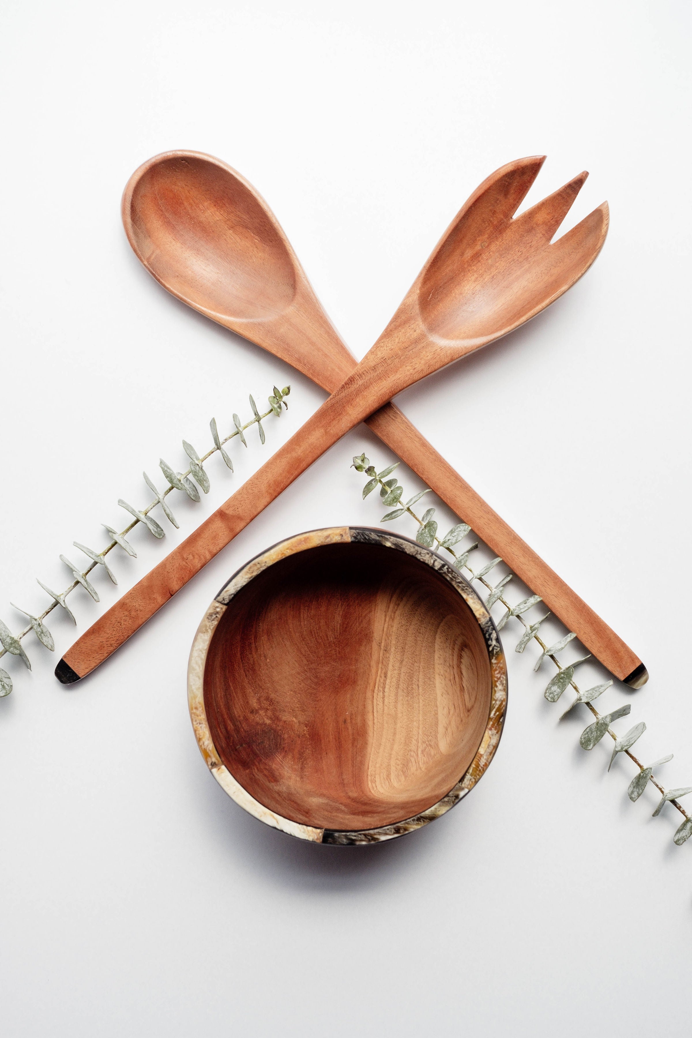 The Suzy Salad Servers, with horn-tipped handles, are elegantly displayed against a white background, complemented by sprigs of eucalyptus.