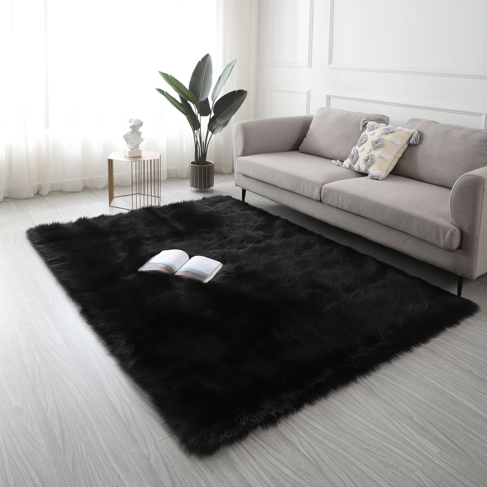 A modern living room featuring a large, Cozy Ultra Soft Fluffy Faux Fur Black Area Rug with an open book on it, a tan sofa, and a side table with a potted plant, against a backdrop of sheer