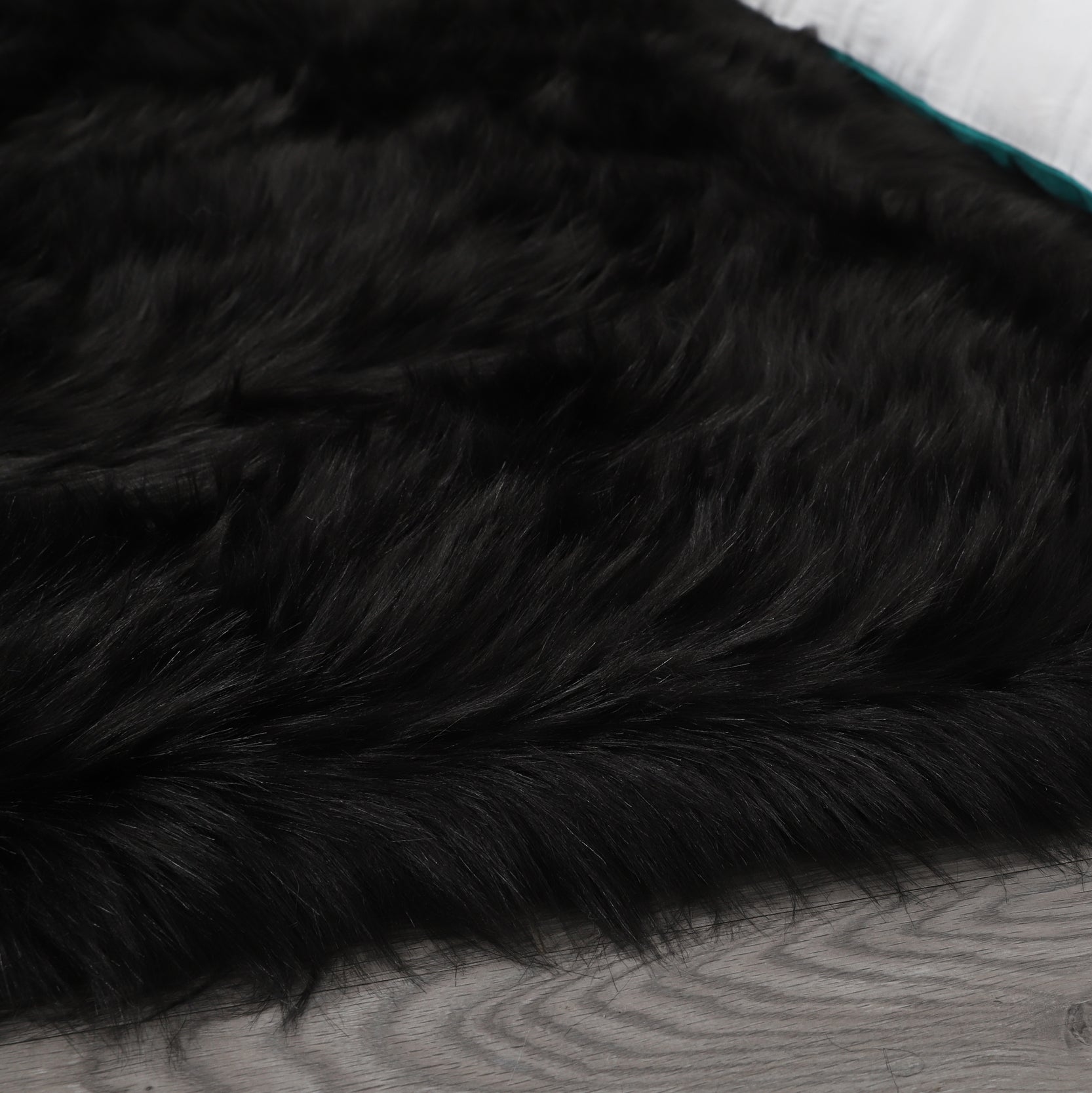 A modern living room featuring a large, Cozy Ultra Soft Fluffy Faux Fur Black Area Rug with an open book on it, a tan sofa, and a side table with a potted plant, against a backdrop of sheer