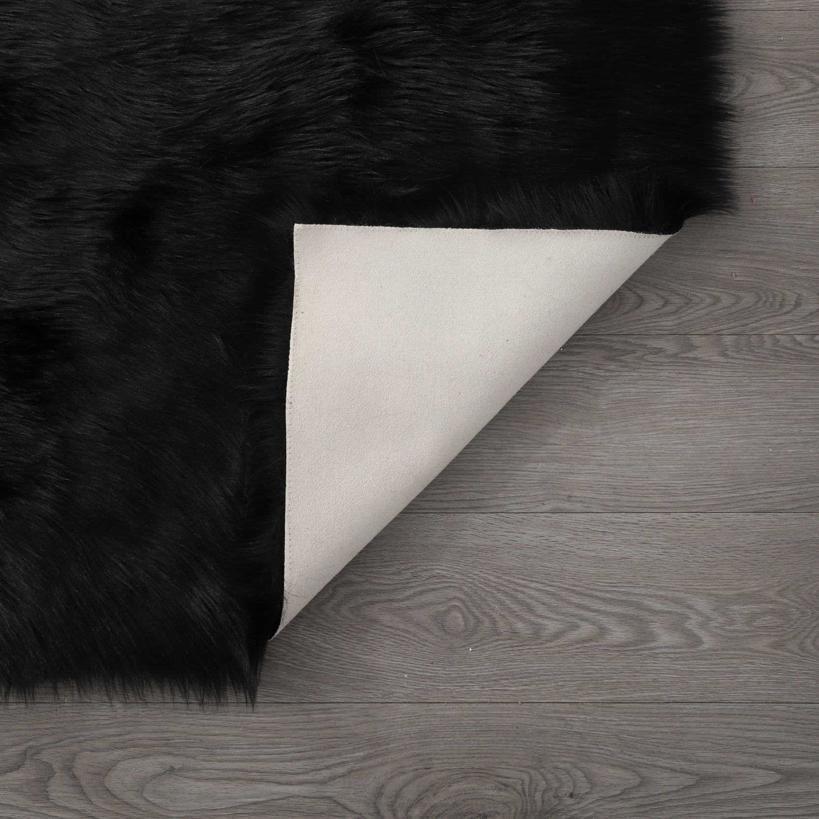 A modern living room featuring a large, Cozy Ultra Soft Fluffy Faux Fur Black Area Rug with an open book on it, a tan sofa, and a side table with a potted plant, against a backdrop of sheer