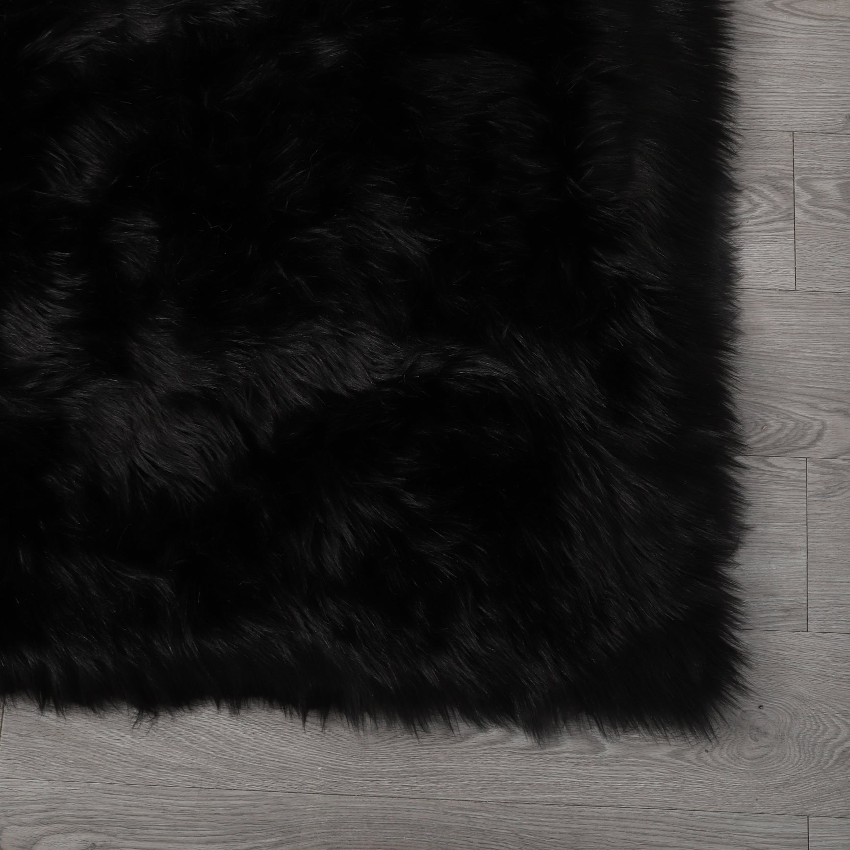 A modern living room featuring a large, Cozy Ultra Soft Fluffy Faux Fur Black Area Rug with an open book on it, a tan sofa, and a side table with a potted plant, against a backdrop of sheer