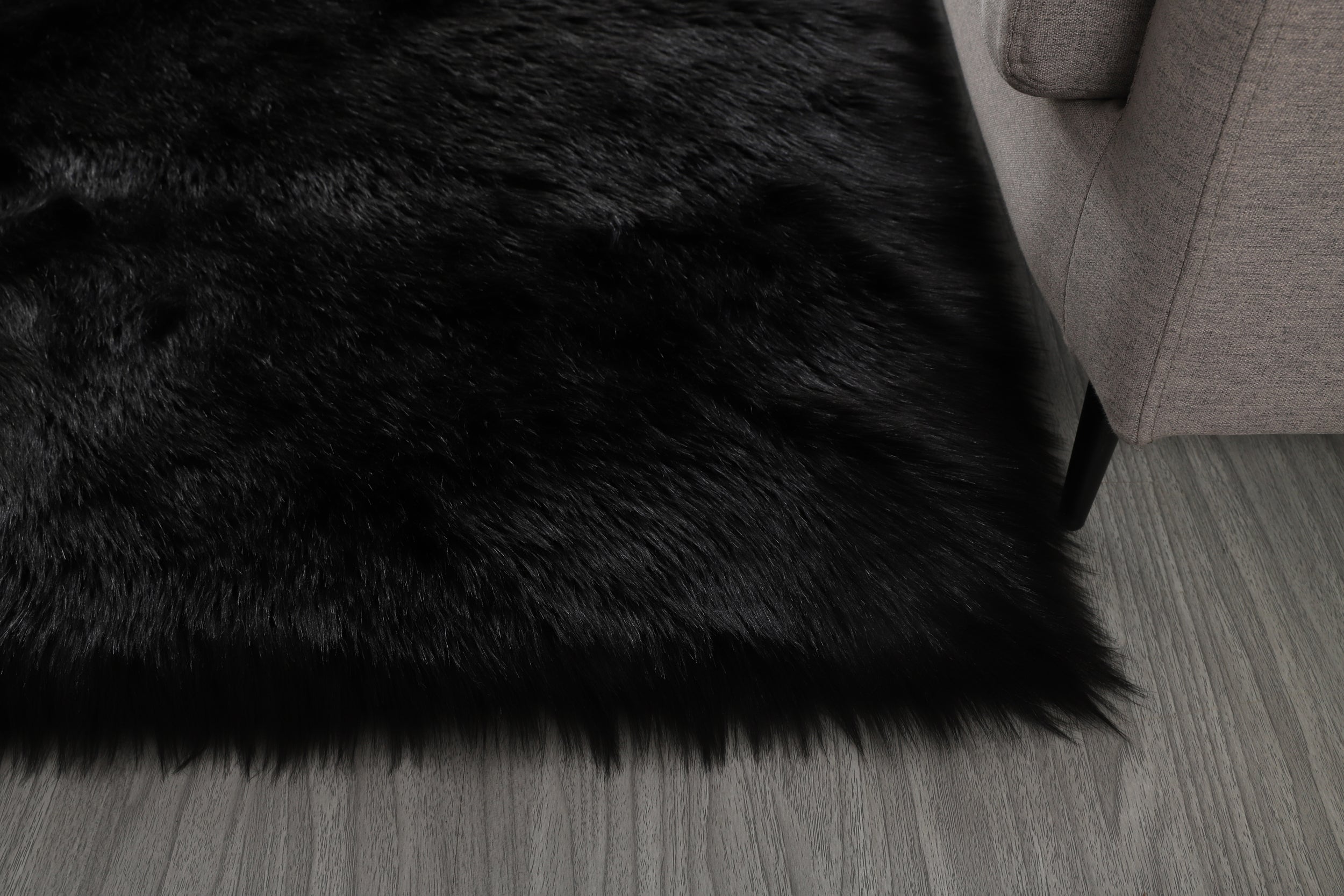 A modern living room featuring a large, Cozy Ultra Soft Fluffy Faux Fur Black Area Rug with an open book on it, a tan sofa, and a side table with a potted plant, against a backdrop of sheer
