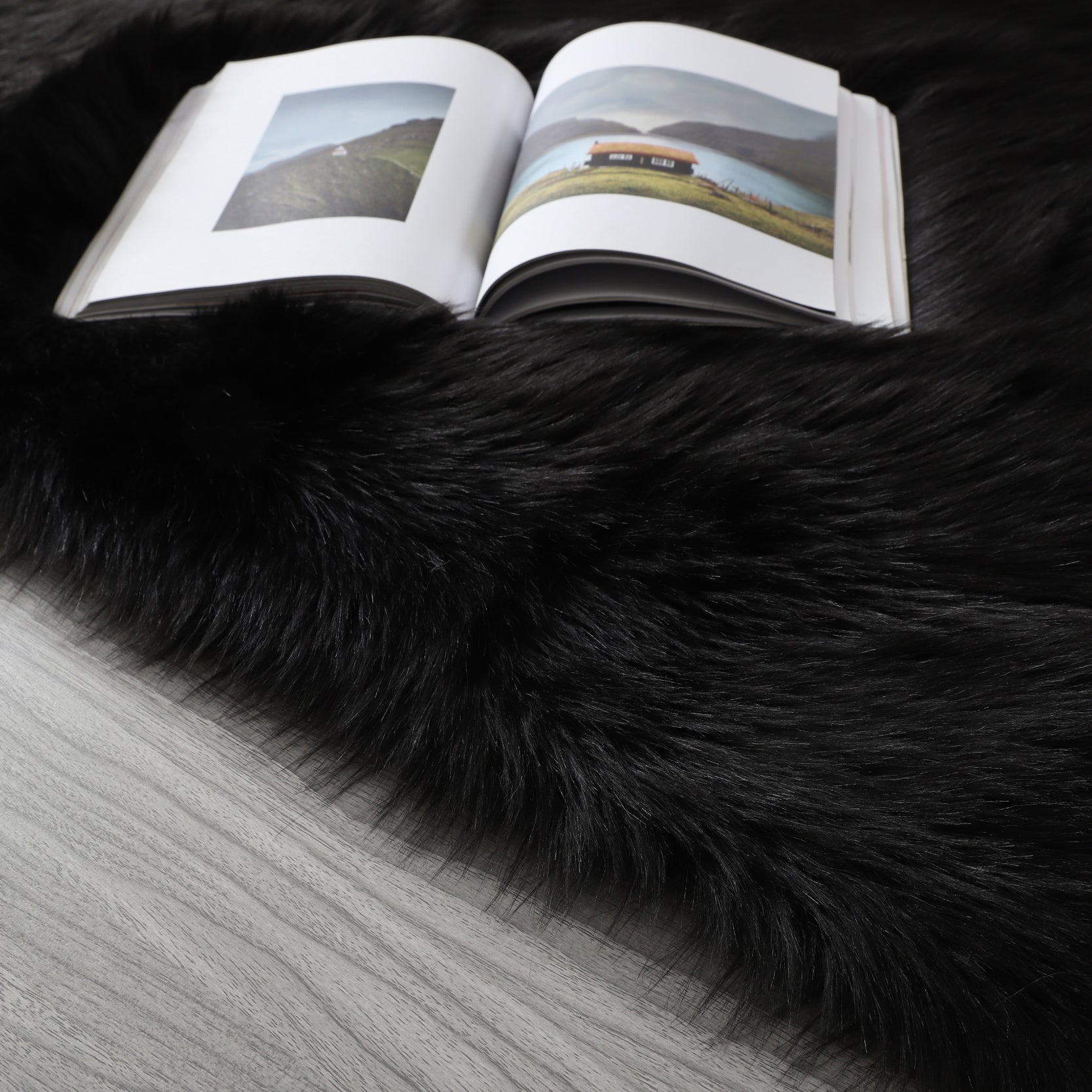 A modern living room featuring a large, Cozy Ultra Soft Fluffy Faux Fur Black Area Rug with an open book on it, a tan sofa, and a side table with a potted plant, against a backdrop of sheer