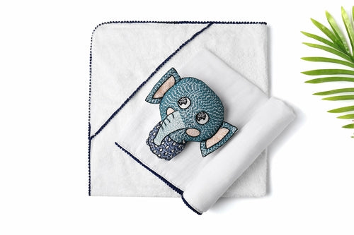 A white 3 Pc Newborn Essential Set - Hooded Towel, Swaddle + Toy Rattle by Ivory Meleager on top of a bed.