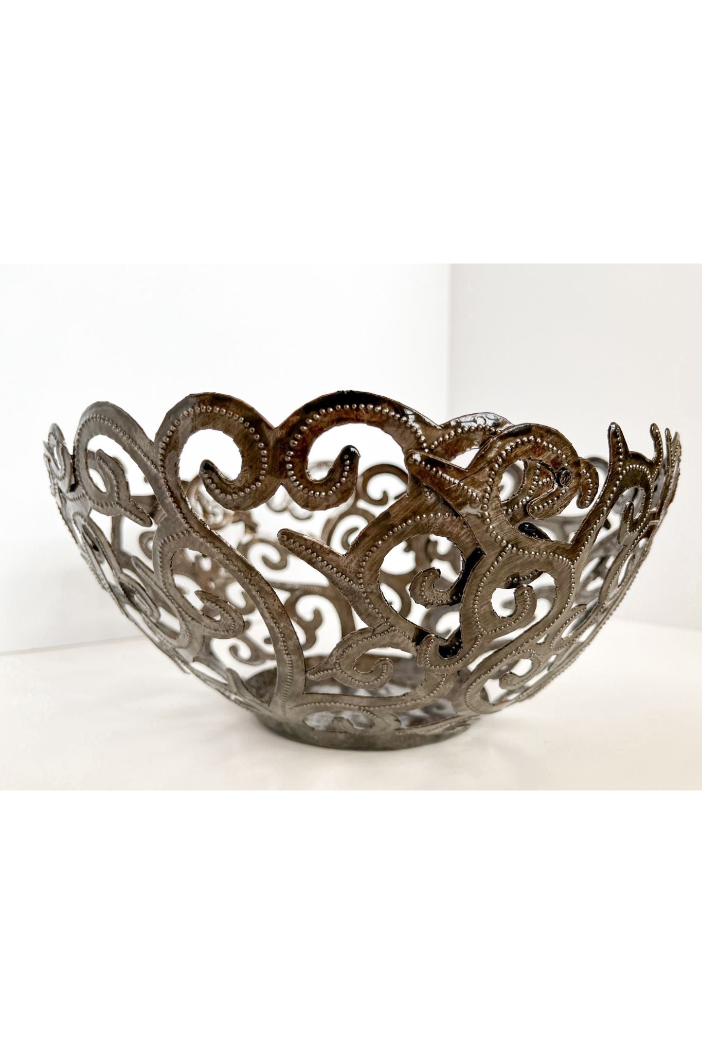 The Metal Art Scroll Bowl, intricately designed with swirling cut-out patterns and crafted from recycled steel, is elegantly displayed on a white surface.