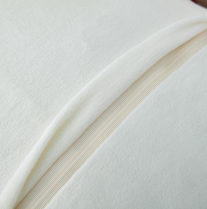 A fluffy white Agnes Luxury Beige Chinchilla Faux Fur Pillow on a cream sofa, with a green plant and white wall in the background.