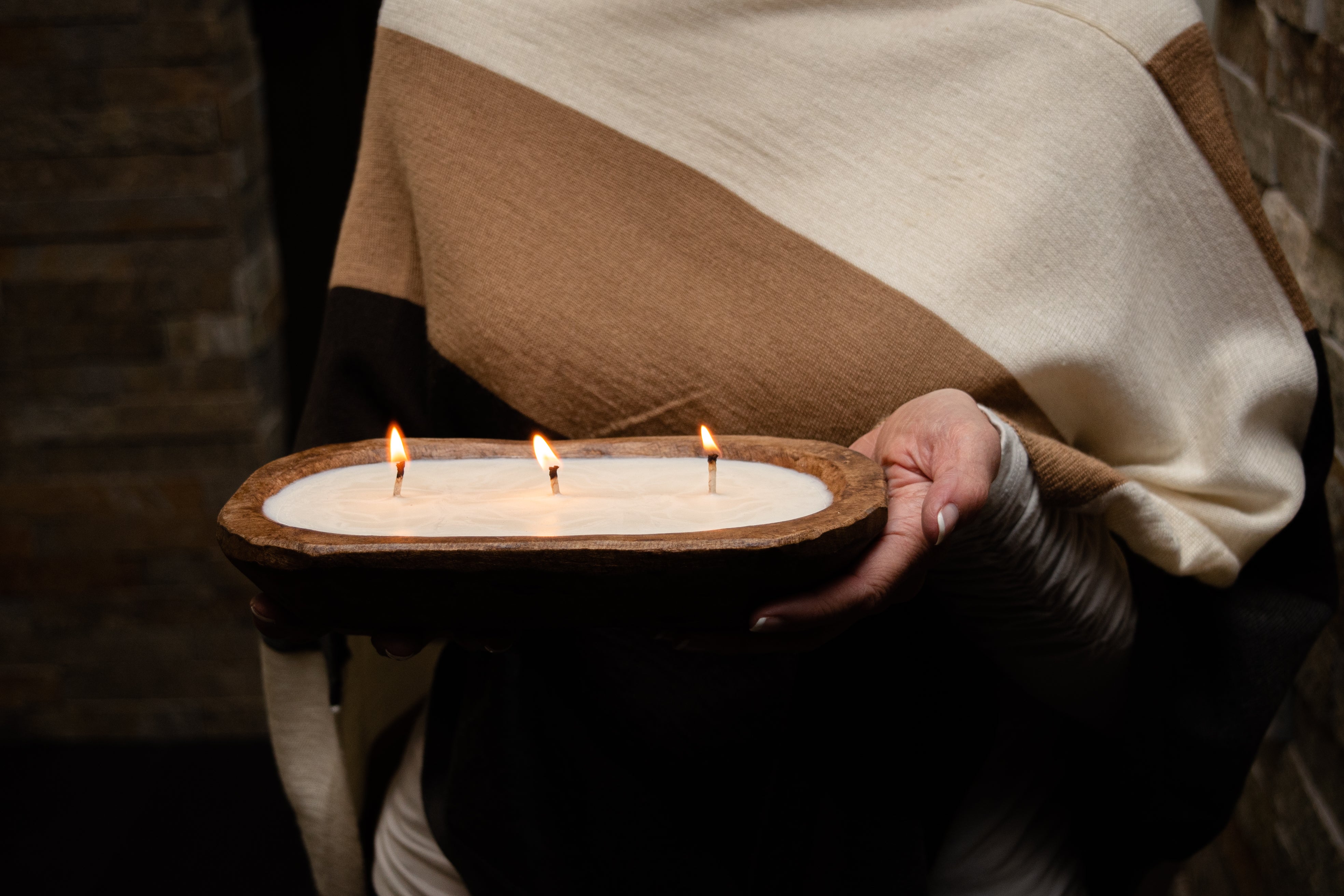 A luxurious 3-wick candle holder made from wood showcases three radiant candles surrounded by verdant foliage. The inscription reads "Amber Noir: Notes - Cedar, Sandalwood & Amber," embodying the elegance of our 3-Wick Dough Bowl Soy Candle - Amber Noir collection.