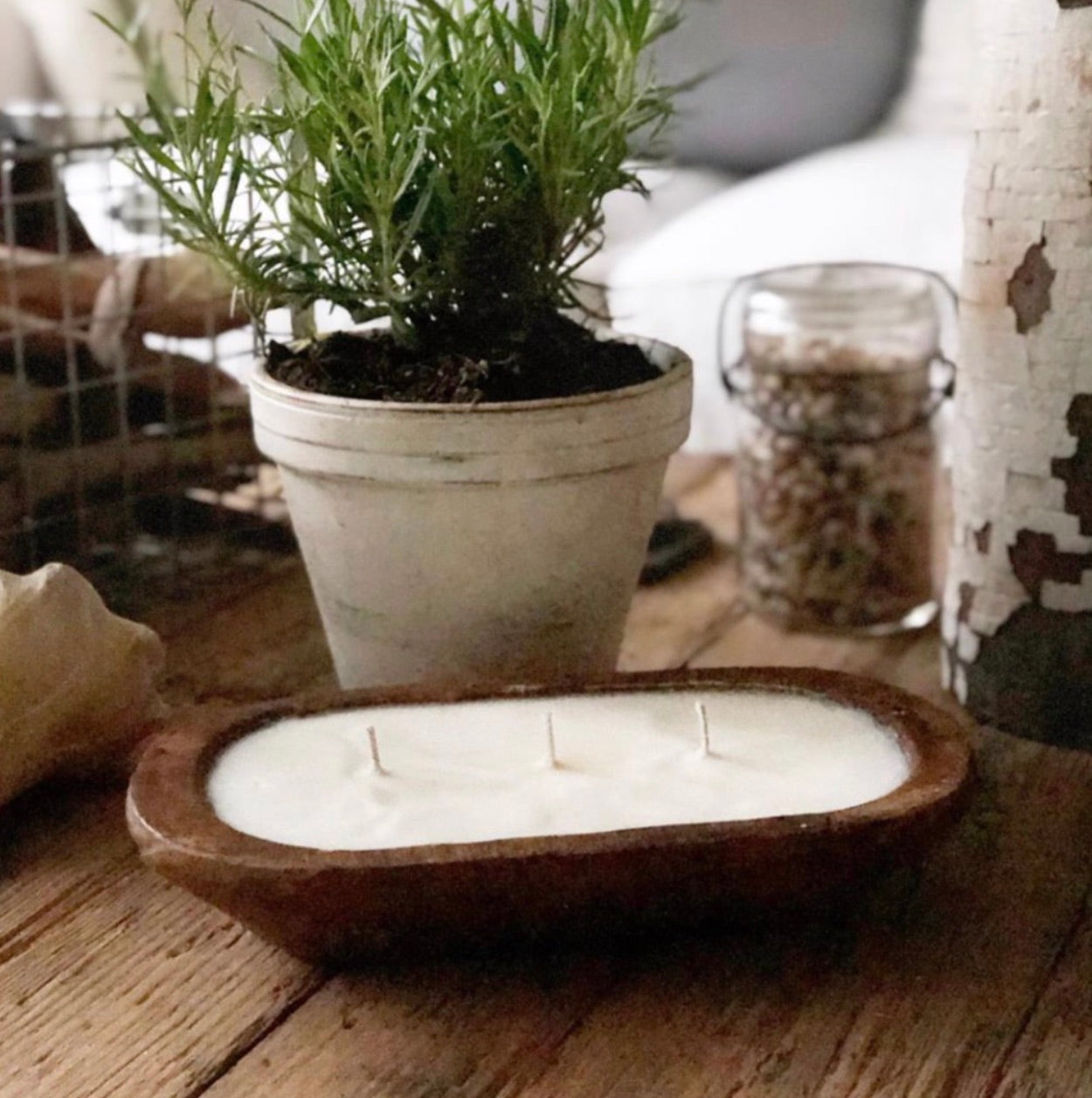 A luxurious 3-wick candle holder made from wood showcases three radiant candles surrounded by verdant foliage. The inscription reads "Amber Noir: Notes - Cedar, Sandalwood & Amber," embodying the elegance of our 3-Wick Dough Bowl Soy Candle - Amber Noir collection.