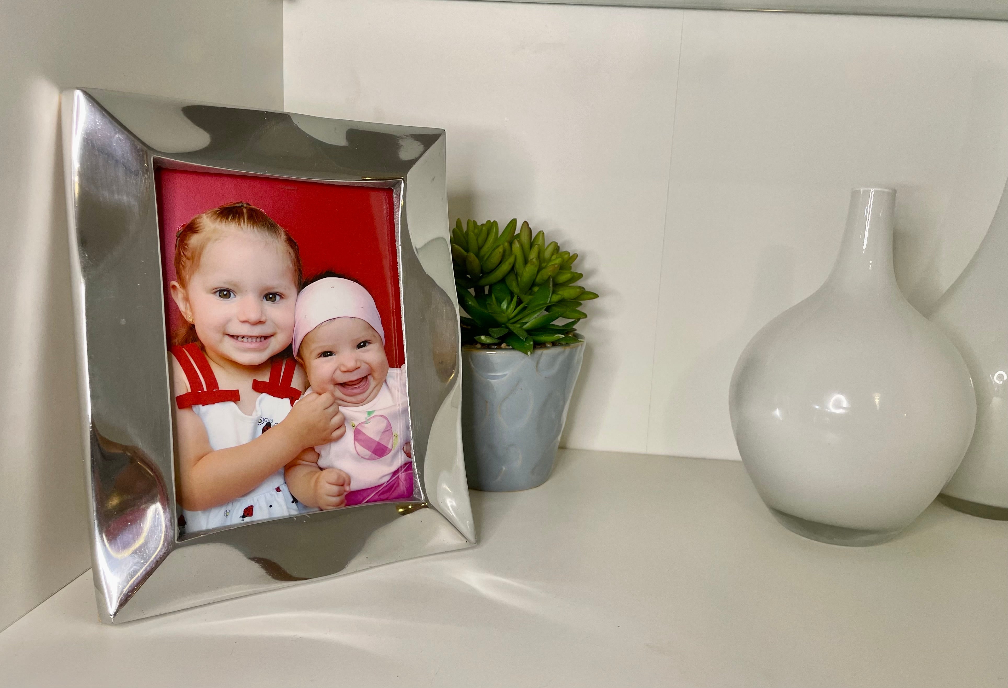 The Stylish Picture Frame is a minimalist design crafted from recycled aluminum, showcasing a silver finish with a plain brown backing and supported by a wooden stand at the back.