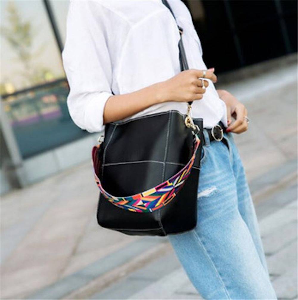 A woman sits on a bench, placing a Threaded Pear wristlet into her large Jordyn Handbag.