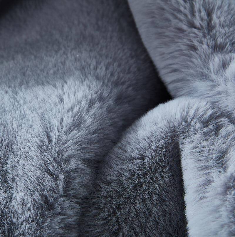 A stain-resistant Cassilda Luxury Grey Chinchilla Faux Fur Throw Blanket draped over a gray sofa in a room with wooden flooring.