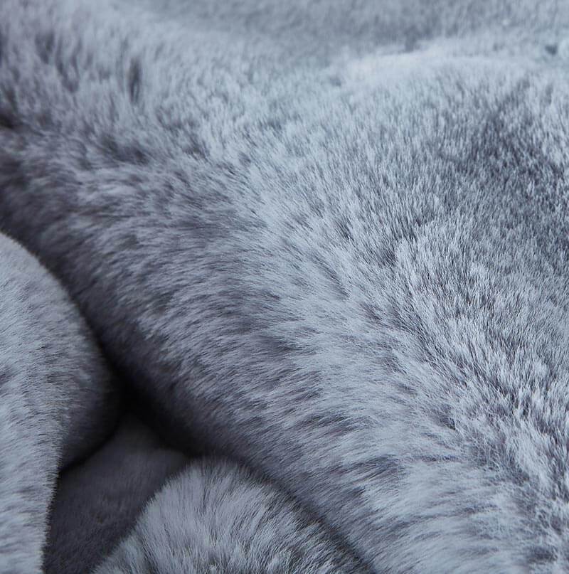 A stain-resistant Cassilda Luxury Grey Chinchilla Faux Fur Throw Blanket draped over a gray sofa in a room with wooden flooring.