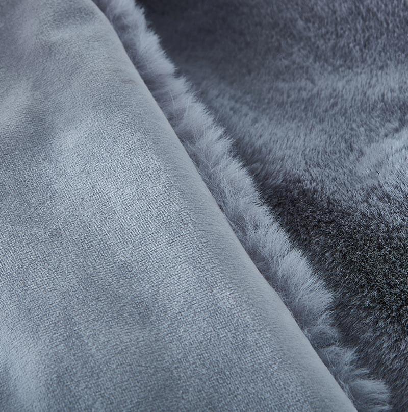 A stain-resistant Cassilda Luxury Grey Chinchilla Faux Fur Throw Blanket draped over a gray sofa in a room with wooden flooring.