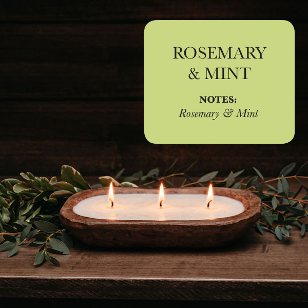 A luxurious 3-Wick Dough Bowl Soy Candle - Rosemary & Mint is elegantly displayed on a wooden surface, surrounded by greenery. The accompanying text reads: "Rosemary & Mint," emphasizing the sophistication of these scented candles.