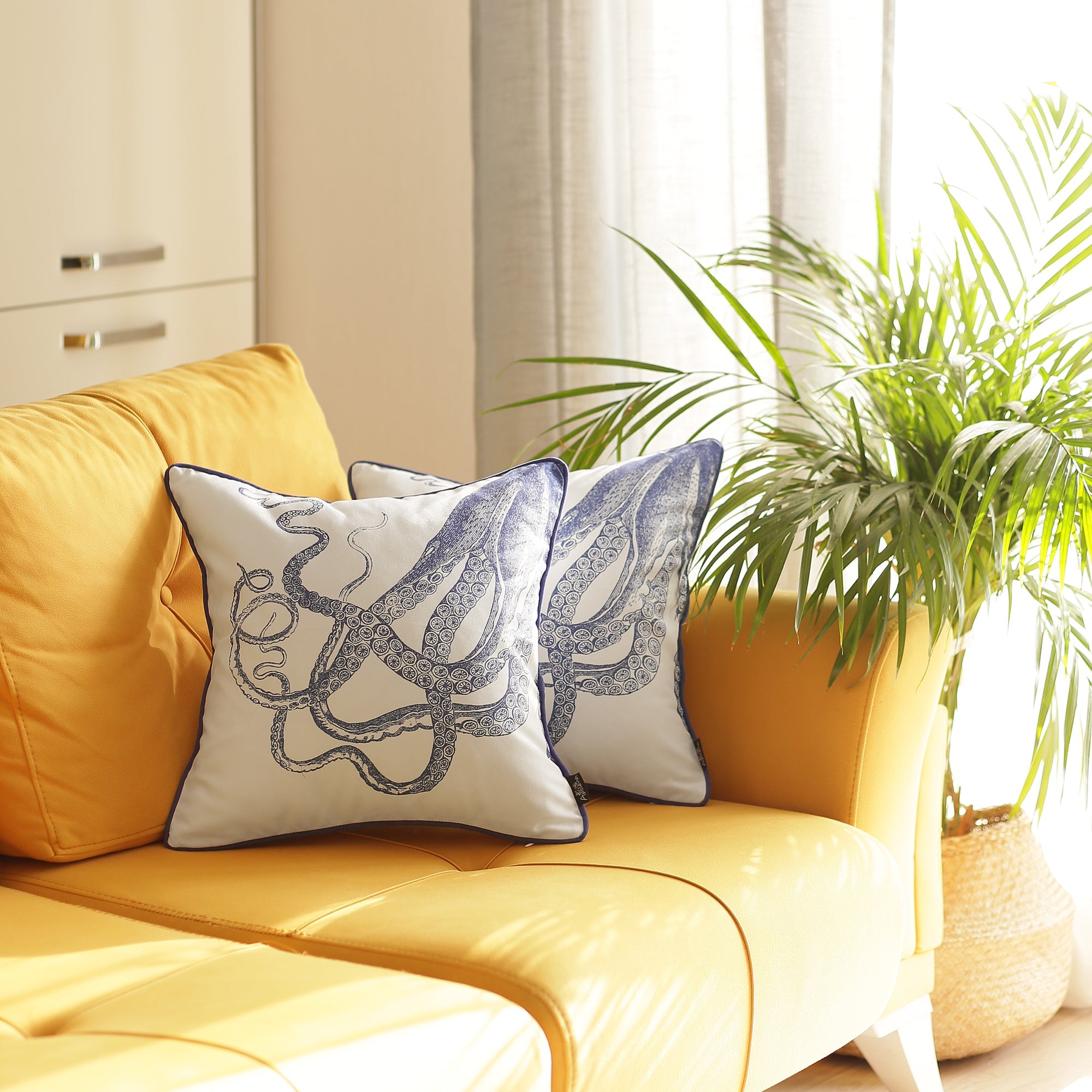 A set of two Nautica Octopus 18" square throw pillow covers, showcasing high-quality digital prints of blue octopus designs, rests on a yellow sofa. With their hidden zipper closures, these decorative covers perfectly complement the green indoor plant in the sunlit room.