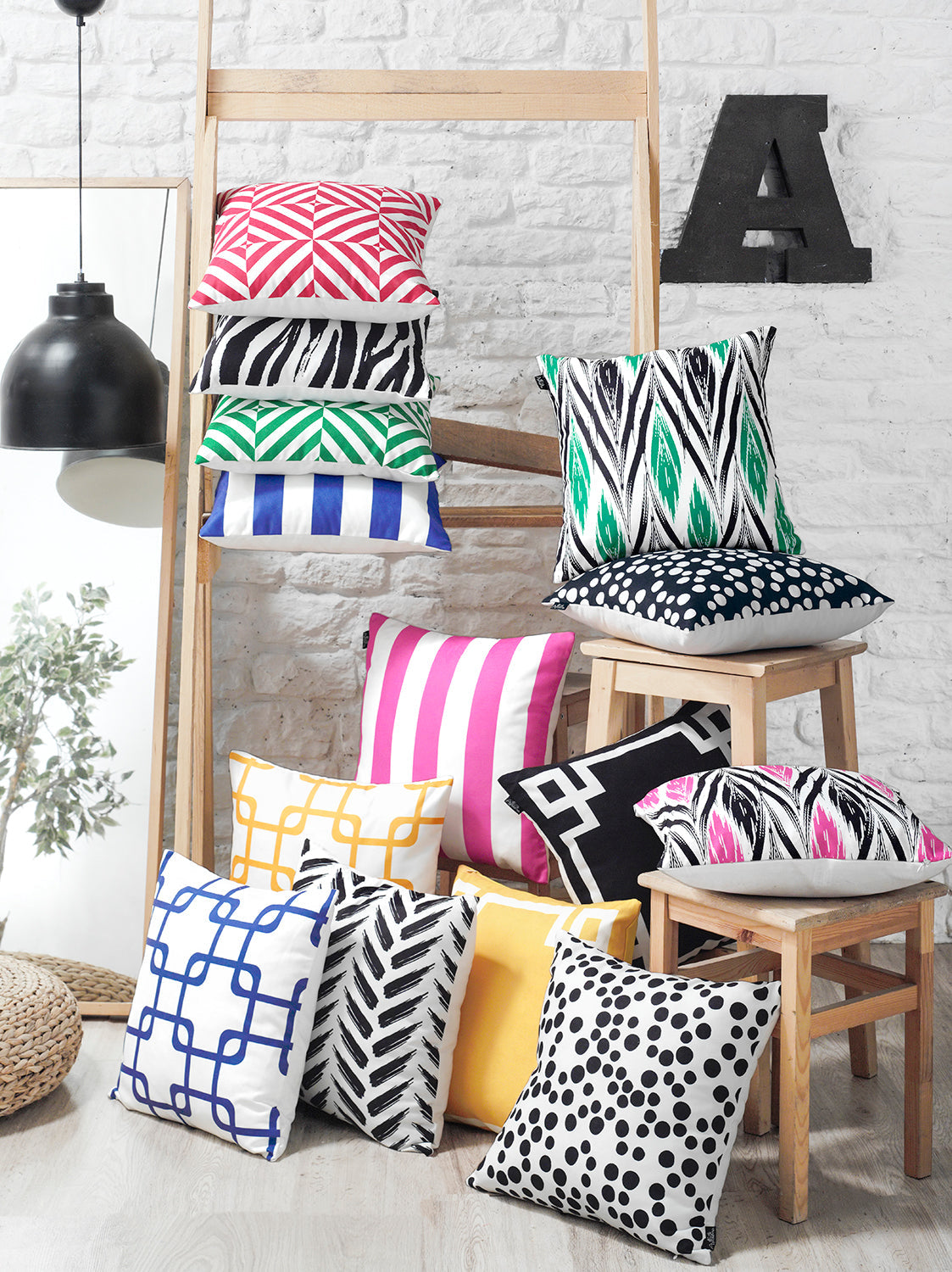 A brown sofa, adorned with the Geometric Black&White Square Decorative Throw Pillow Covers (Set of 2), featuring bold black and white geometric patterns, is positioned next to a potted plant and a bookshelf. Each pillow cover includes a hidden zipper closure for easy maintenance.