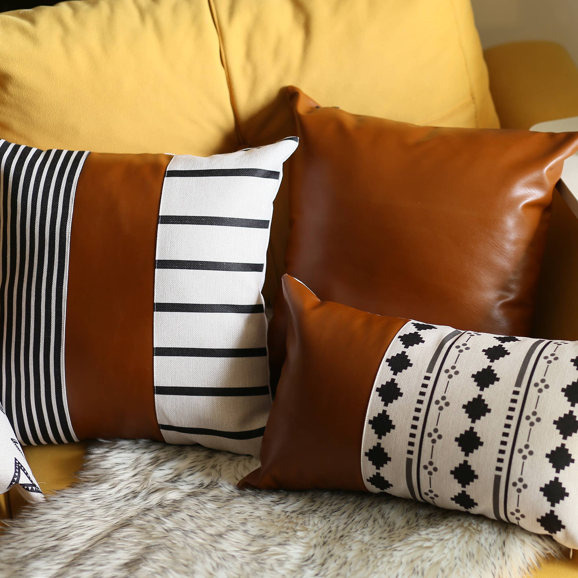 A pair of decorative pillows, featuring one in orange and another with a geometric design, are placed on a gray sofa in a modern living room. The Boho Set of 2 Handcrafted Decorative Throw Pillow Covers, made from vegan faux leather with geometric patterns, add an artistic flair that enhances the chic and cozy feel of the space.