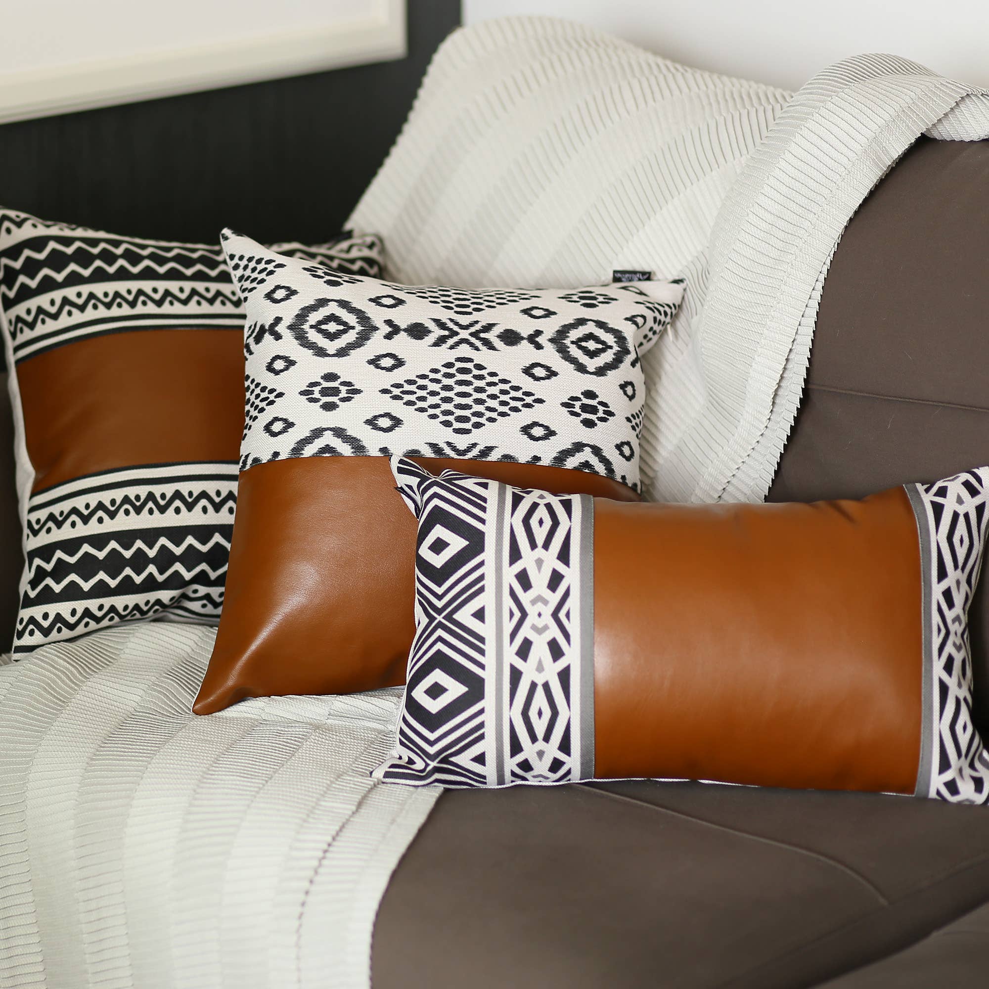 A Boho set of 2 handcrafted decorative throw pillow covers made of vegan faux leather with geometric squares complements a yellow sofa in a sunlit room, enhanced by a striped white blanket and a vibrant potted plant.