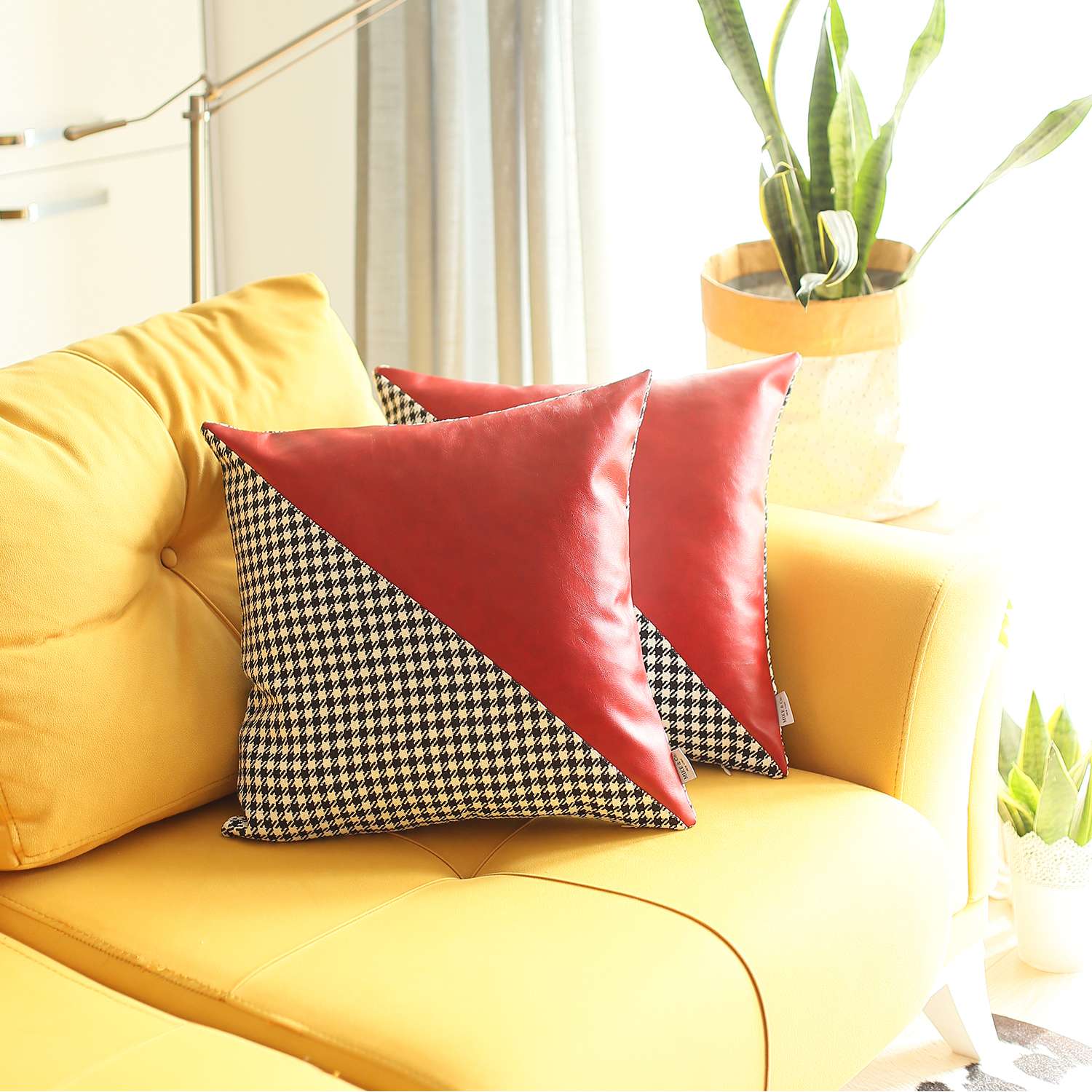 Two boho-chic 18" x 18" square throw pillow covers, handcrafted from vegan faux leather and featuring houndstooth patterns, adorn a brown couch. In the backdrop, a wooden ladder shelf holding a book enhances the cozy atmosphere with its harmonious blend of textures and eclectic design sensibilities.