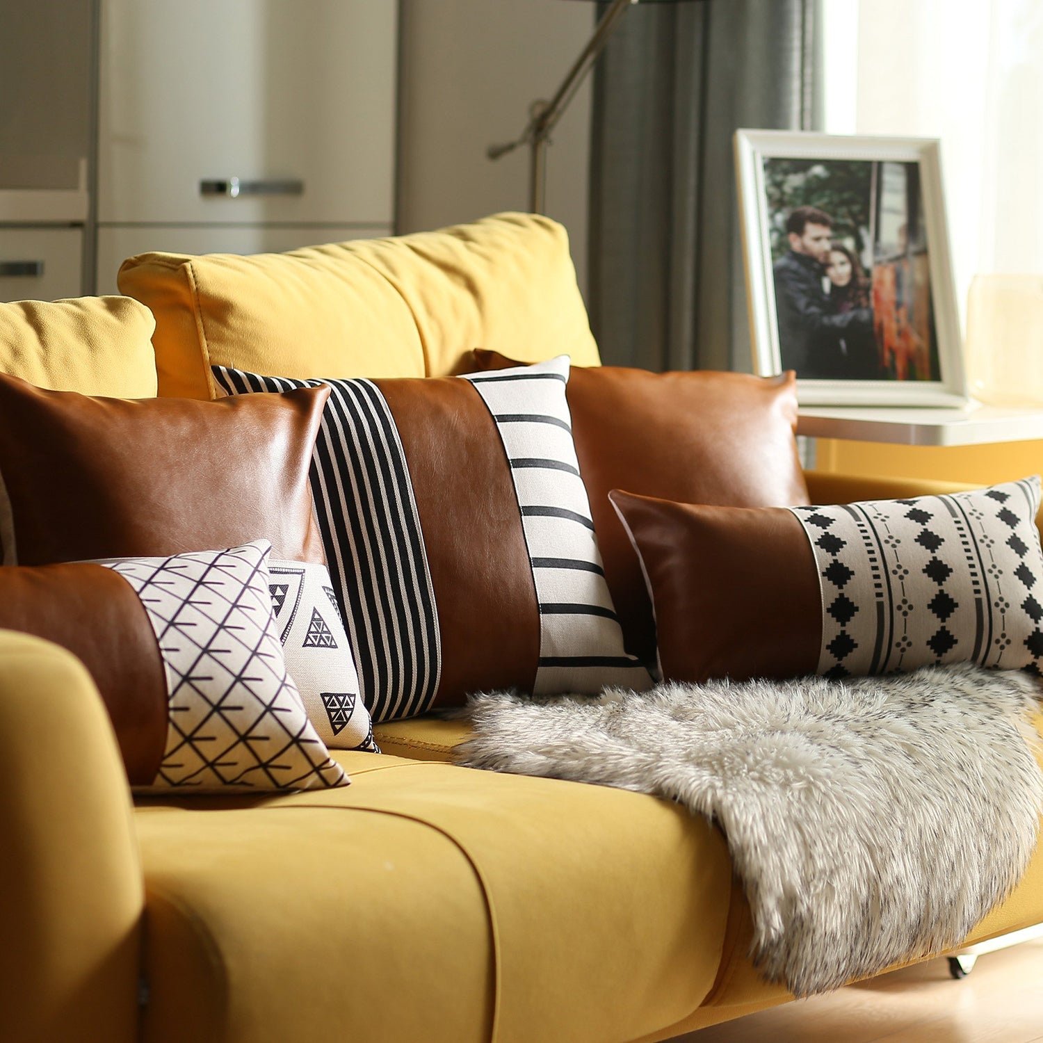 A brown couch decorated with a Bohemian Mixed Set of 2 Vegan Faux Leather Brown Geometric Throw Pillow Covers, enhanced by a knitted blanket and a plant in the background.