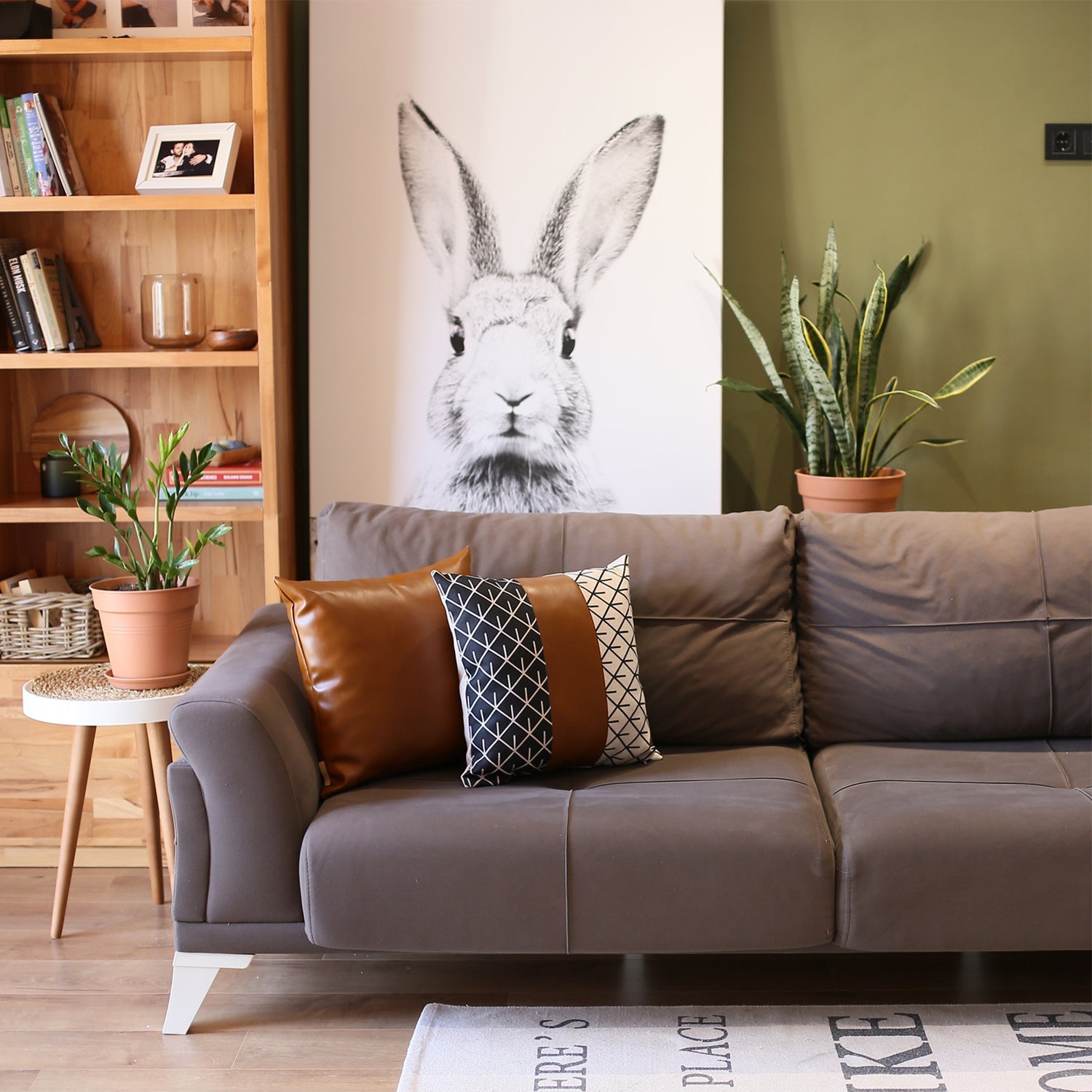 A brown couch decorated with a Bohemian Mixed Set of 2 Vegan Faux Leather Brown Geometric Throw Pillow Covers, enhanced by a knitted blanket and a plant in the background.