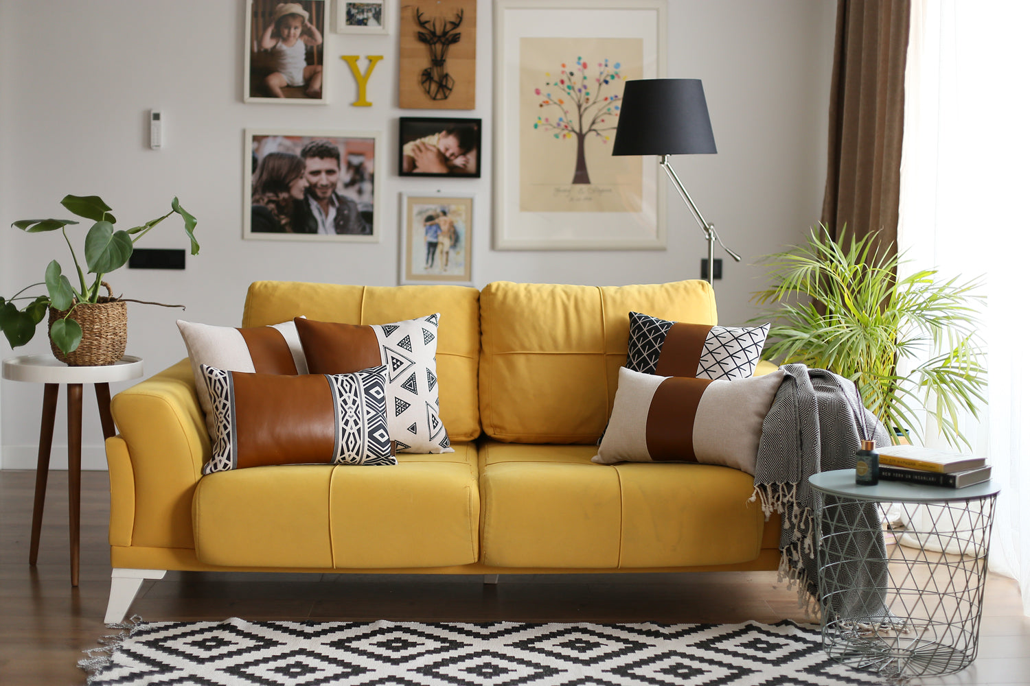 A brown couch decorated with a Bohemian Mixed Set of 2 Vegan Faux Leather Brown Geometric Throw Pillow Covers, enhanced by a knitted blanket and a plant in the background.