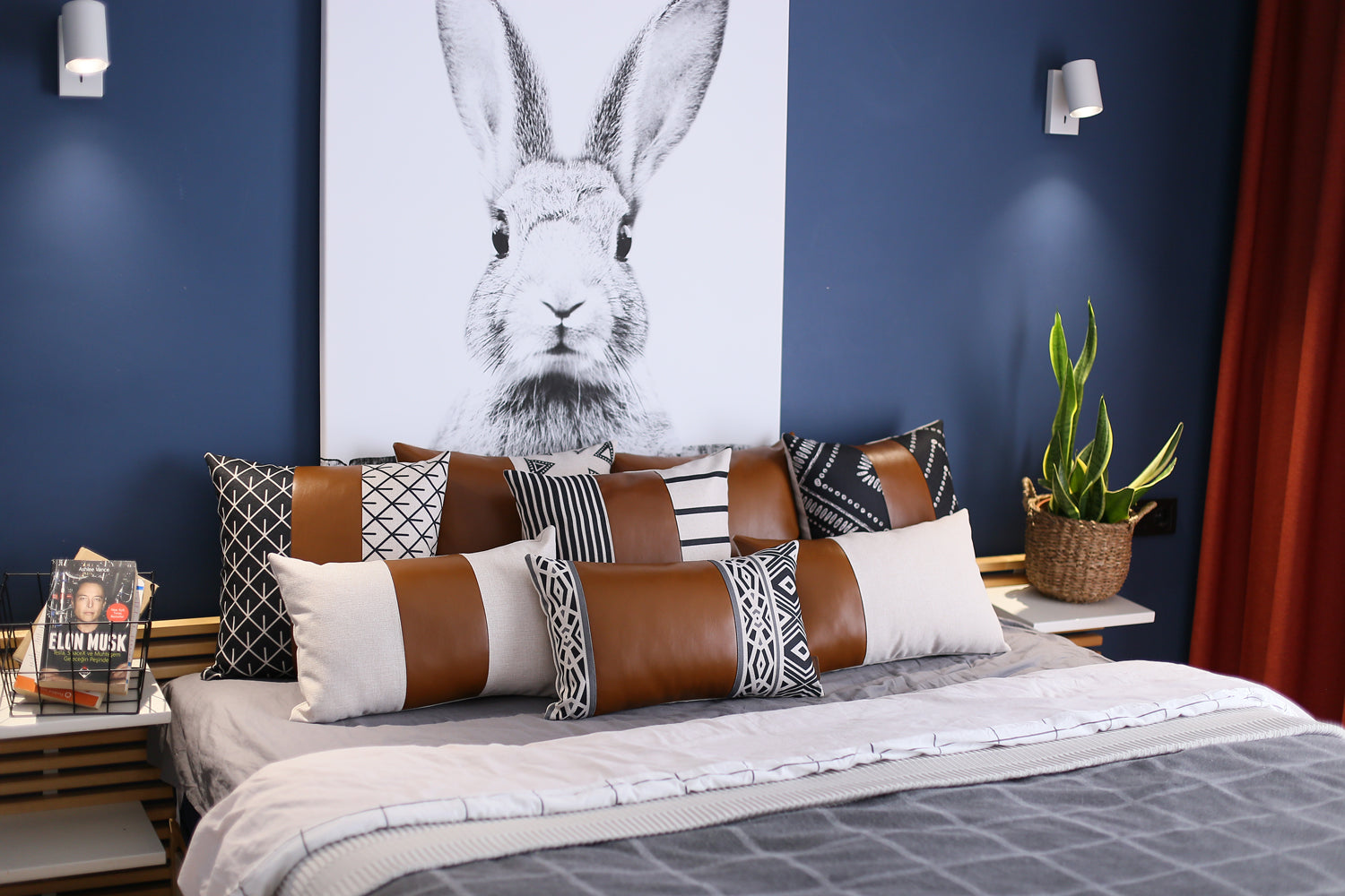 A brown couch decorated with a Bohemian Mixed Set of 2 Vegan Faux Leather Brown Geometric Throw Pillow Covers, enhanced by a knitted blanket and a plant in the background.