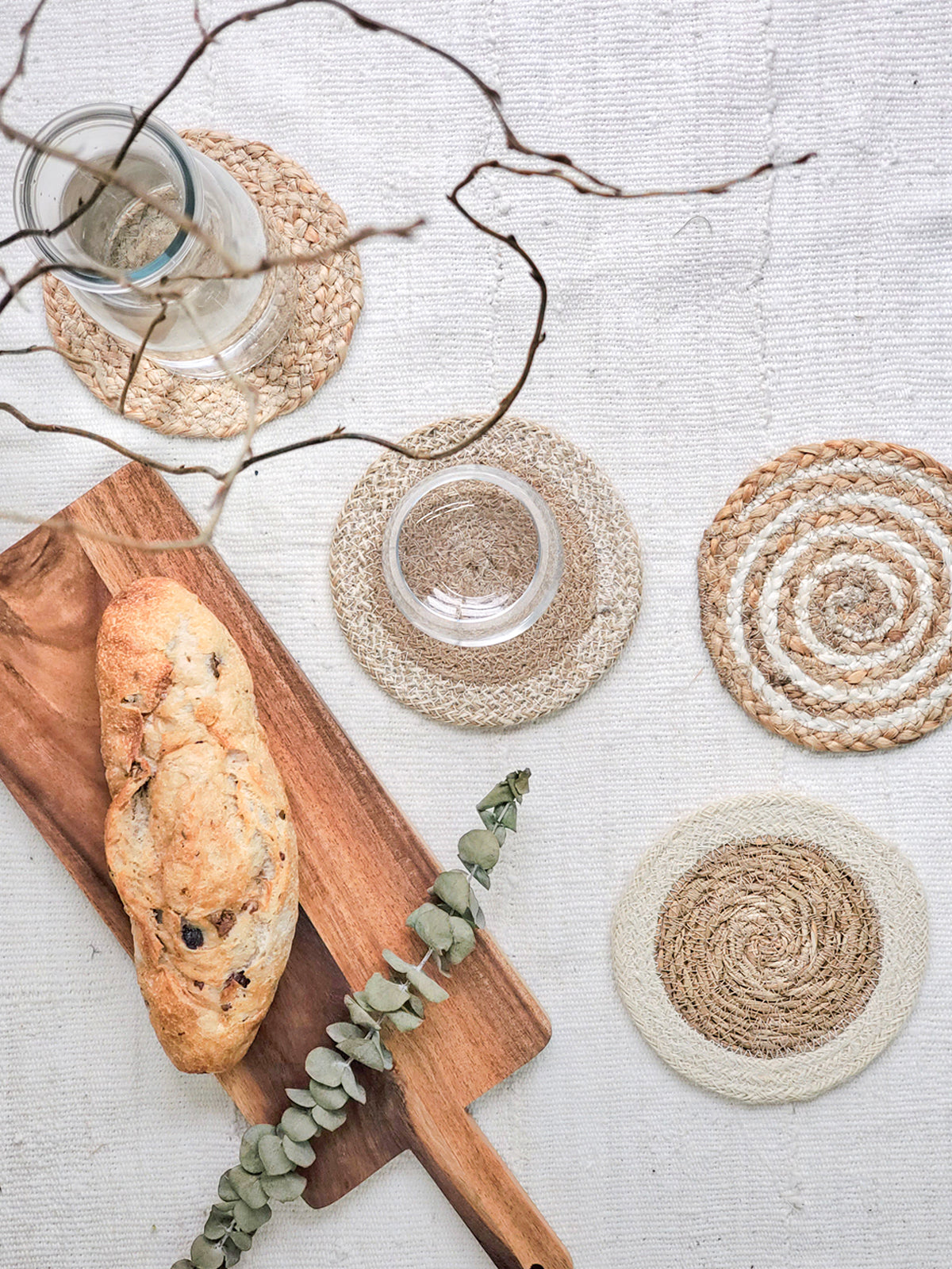 The Natural Coaster Trivet Gift Set with Green Pouch includes a patterned fabric pouch adorned with green tassels, housing five round jute coasters in assorted natural tones, meticulously crafted by Fair Trade artisans.