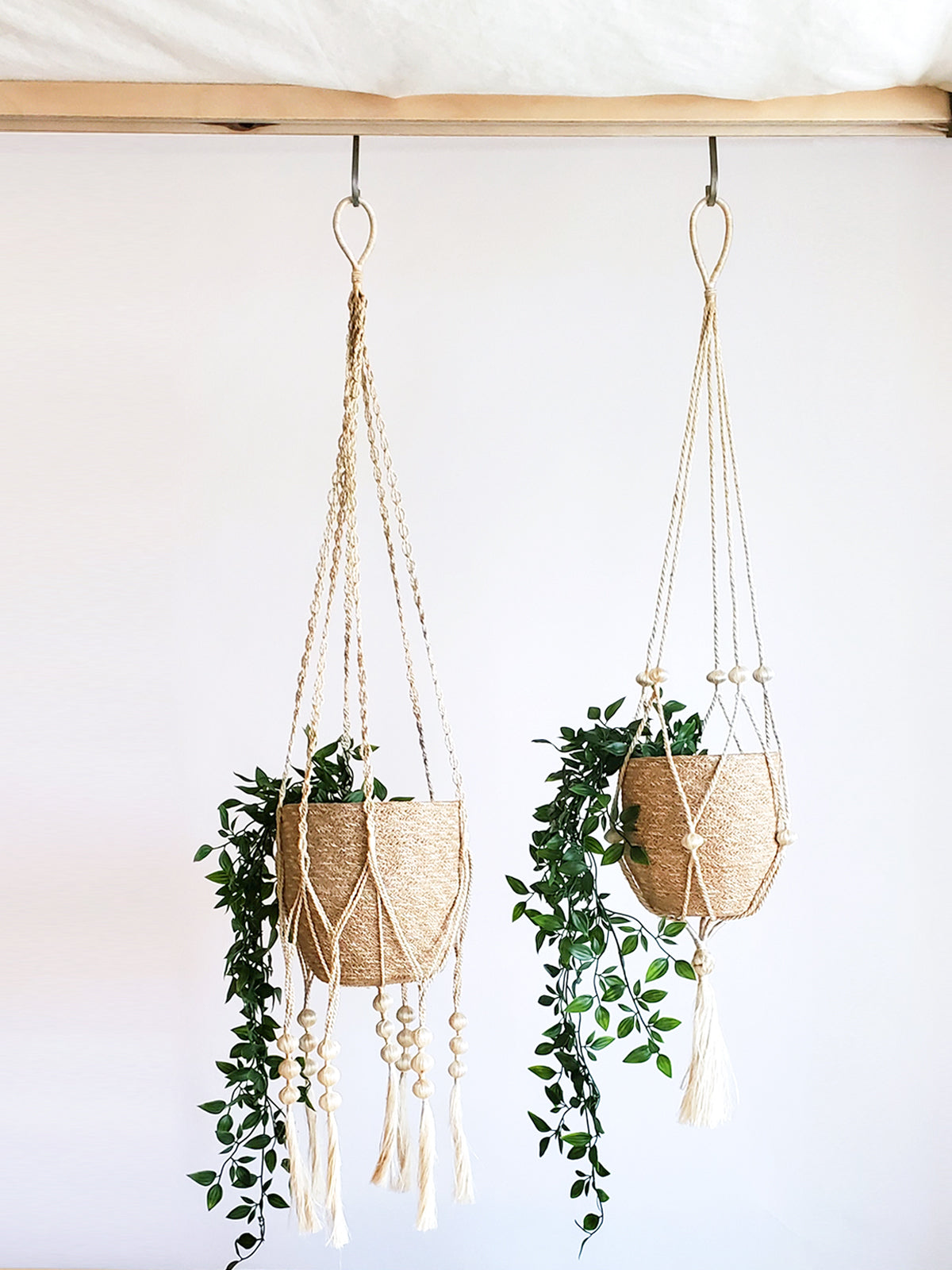 The Plant Hanger - Fiora is a beautiful handmade macramé plant holder, showcasing a black pot adorned with a beige jute rope design, complemented by wooden beads and tassels. Crafted by Fair Trade artisans, it represents sustainable handicraft.