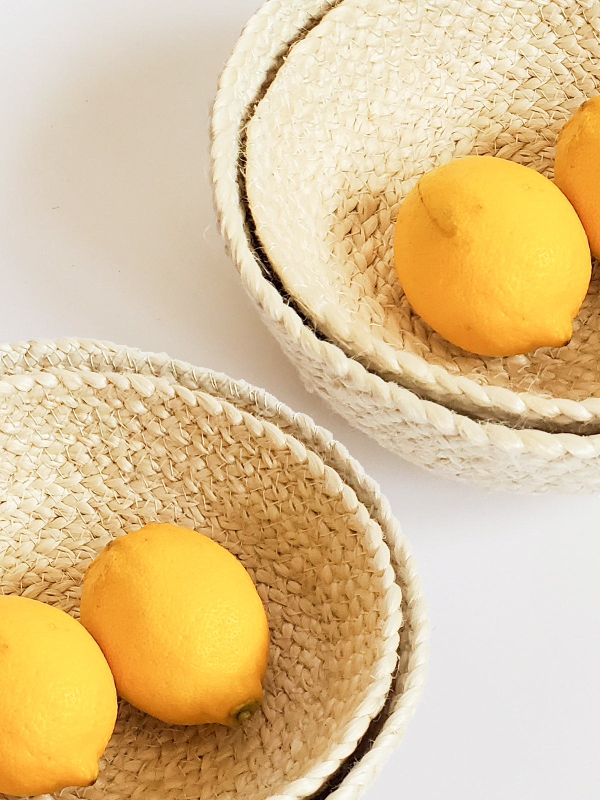 On a flat surface against a plain background, a set of four Kata Candy Bowls in white, crafted by fair trade artisans, is displayed. These versatile woven straw baskets highlight the beauty and authenticity of natural jute.