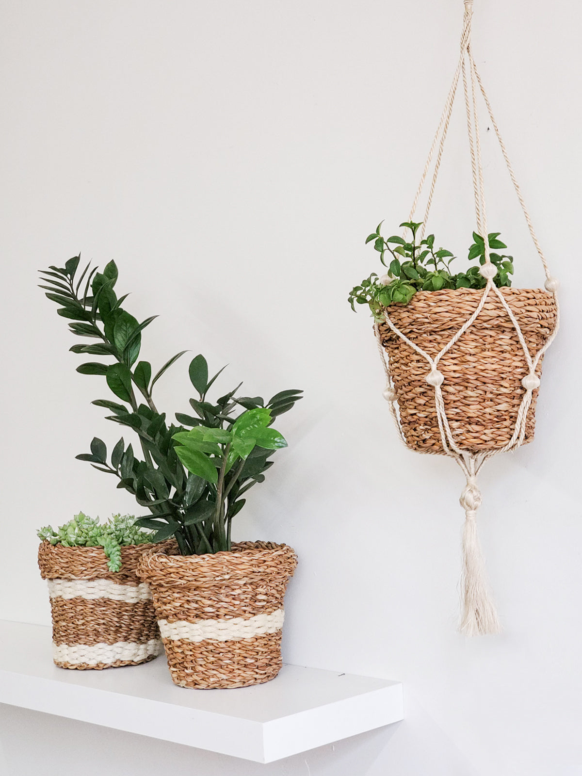 Three Savar Nesting Plant Baskets, crafted by Fair Trade artisans, feature white stripe accents. Two are stacked upright while one lies sideways on a plain background, showcasing their sustainable beauty.