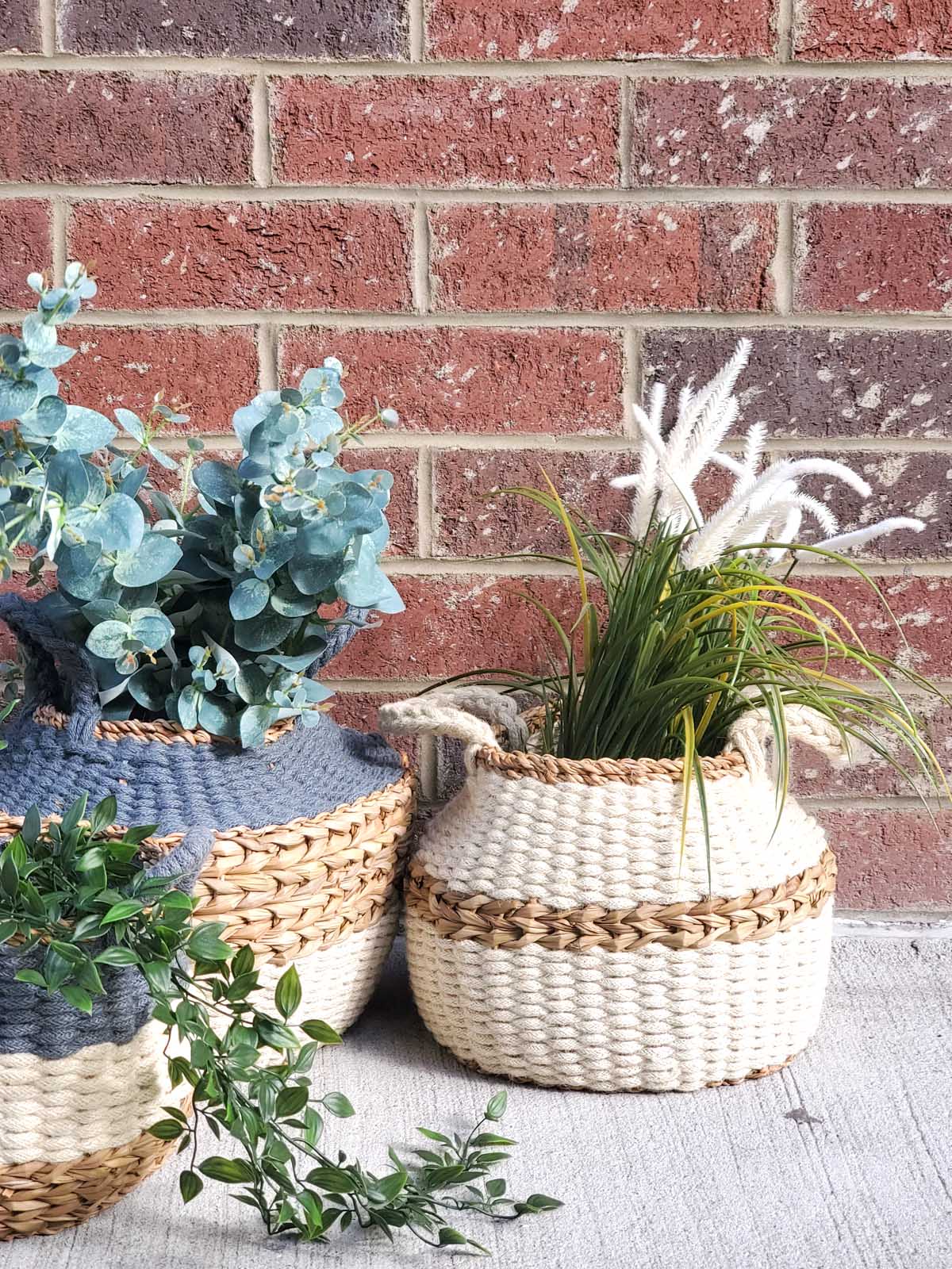 The Ula Blanco Basket is a handwoven piece with two handles, showcasing a natural color and a brown accent stripe around the middle, crafted by sustainable artisans using ethically sourced materials.