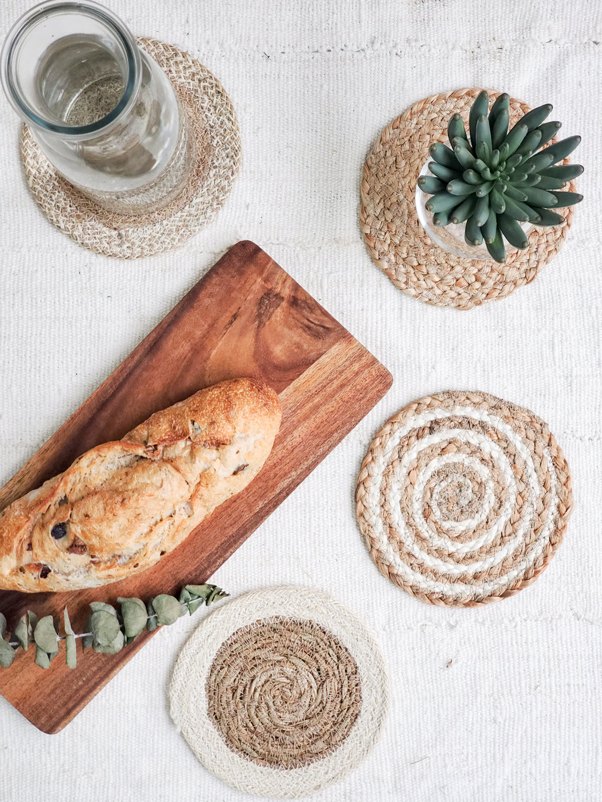 The Natural Coaster Trivet Gift Set with Green Pouch includes a patterned fabric pouch adorned with green tassels, housing five round jute coasters in assorted natural tones, meticulously crafted by Fair Trade artisans.