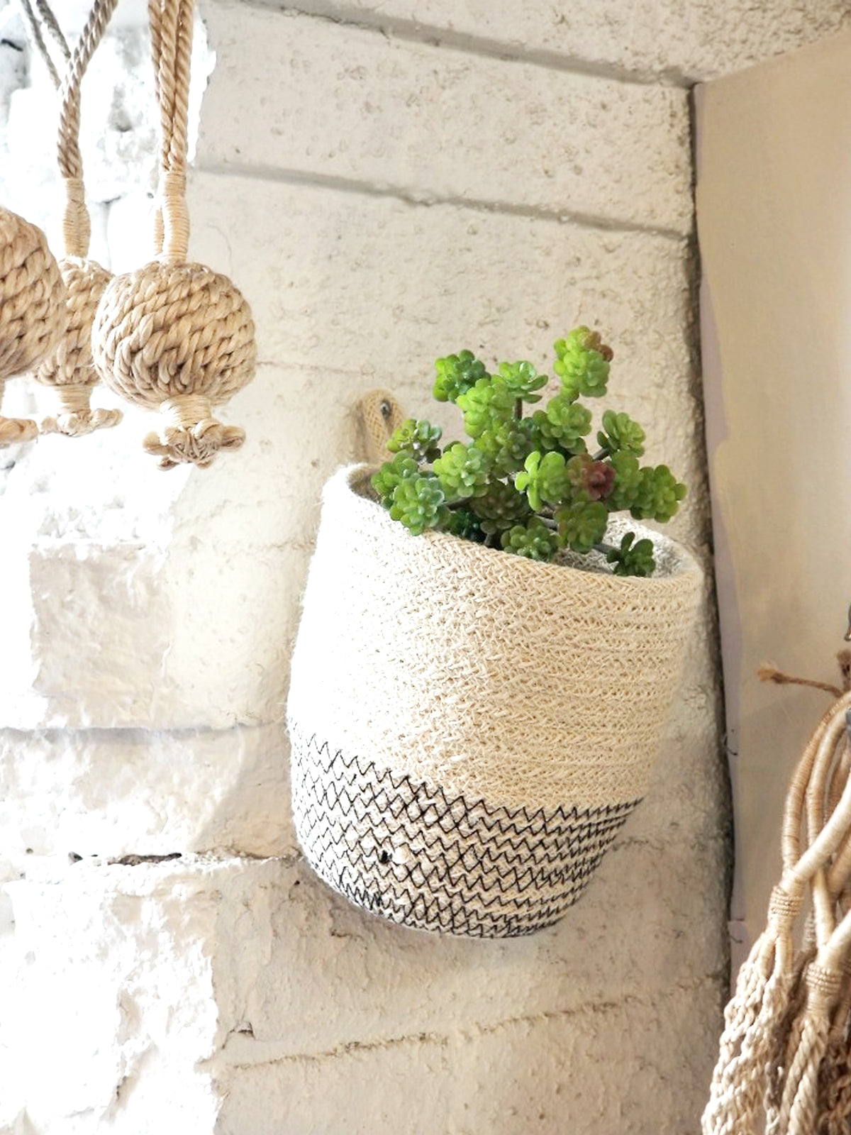 The Amari Loop Bin - Black, a beige and black woven basket featuring a loop handle, is elegantly displayed on a plain white background. Sustainably handmade by Fair Trade artisans, it seamlessly blends style with ethical craftsmanship.