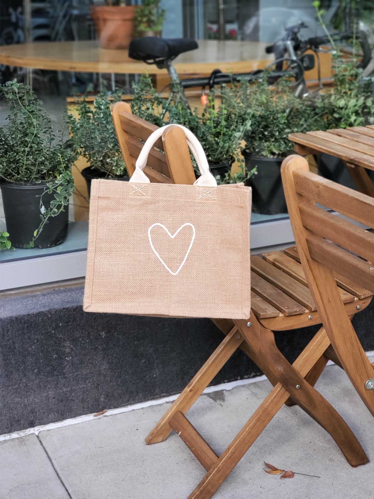 The "Gift Bag - Love" is a beige jute tote bag, handcrafted sustainably with short handles and adorned with a white heart outline on the front.