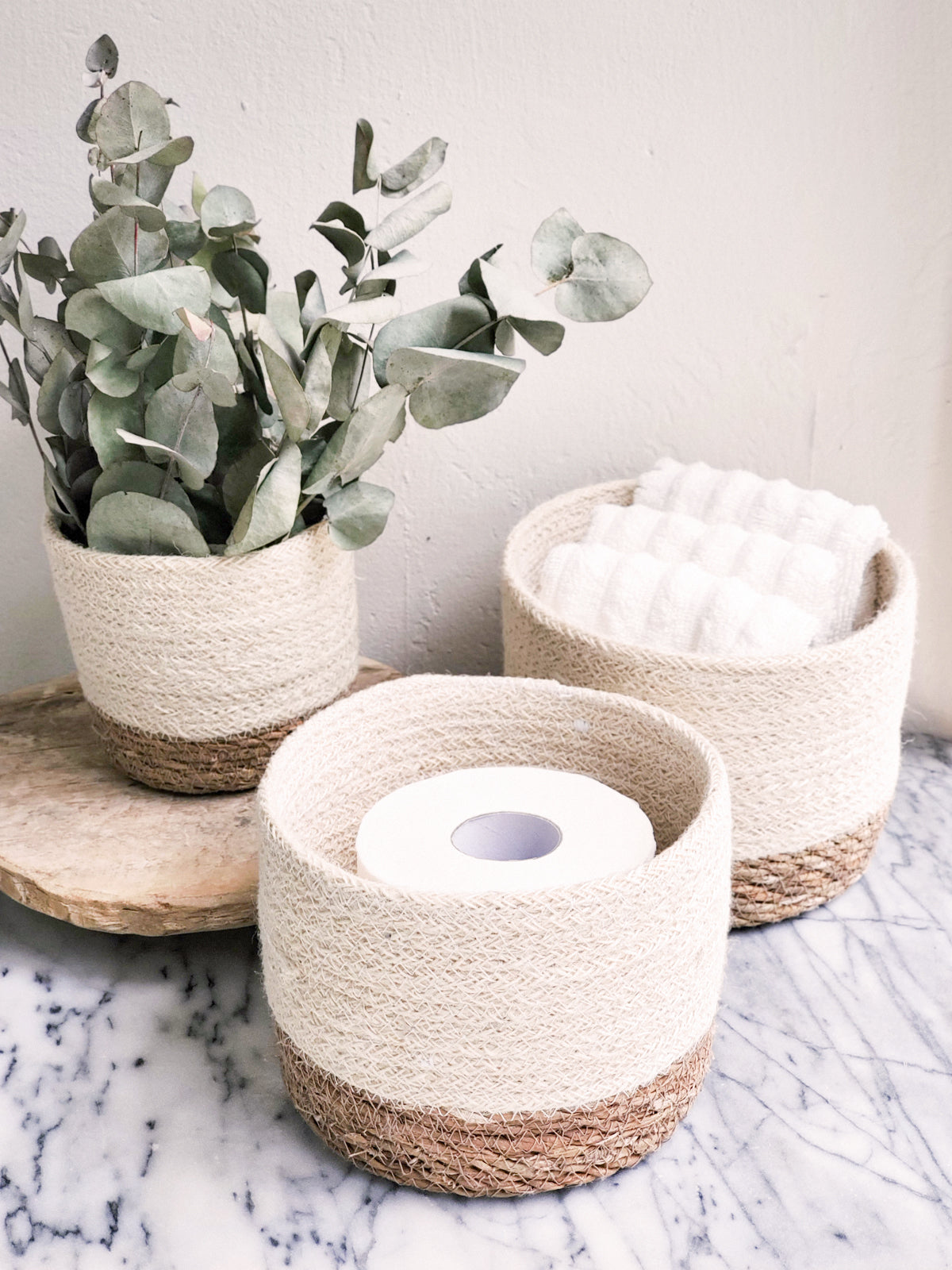 Three Savar Bins, woven sustainably by Fair Trade artisans in varying sizes, each featuring a beige upper half and a brown lower half, are arranged in a row.