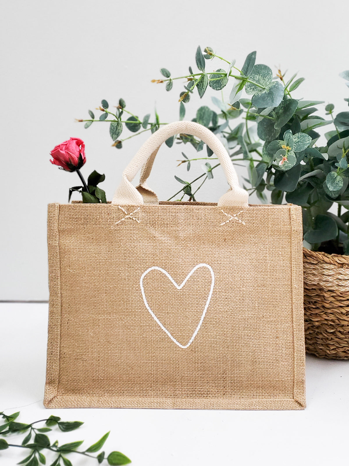 The "Gift Bag - Love" is a beige jute tote bag, handcrafted sustainably with short handles and adorned with a white heart outline on the front.