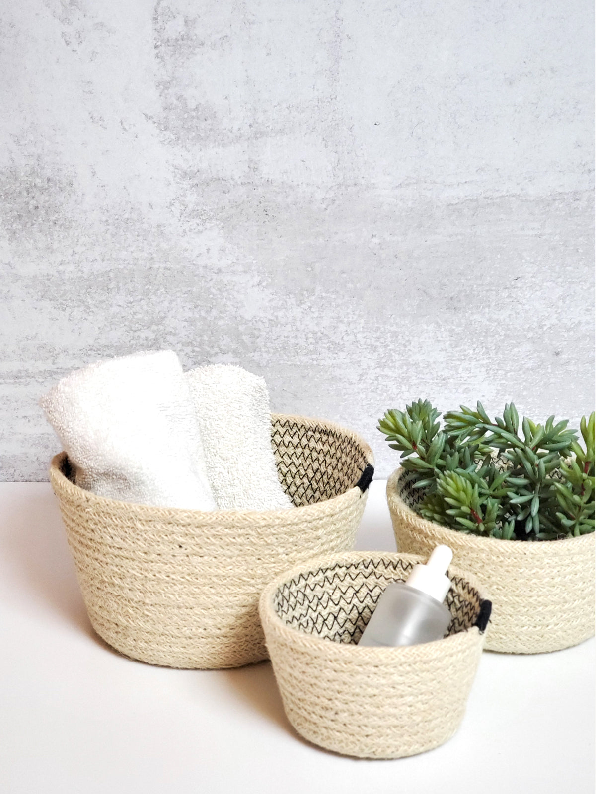 A set of three Amari Bowls in black, handmade beige woven jute baskets of varying sizes by Fair Trade artisans, arranged on a plain background.