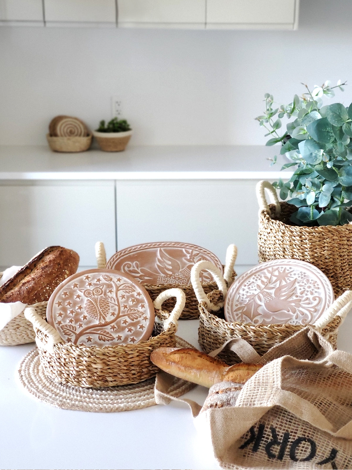 The Bread Warmer & Basket - Owl Round features a sustainably handmade woven basket paired with a round ceramic bread warmer, beautifully adorned with an enchanting owl design among twinkling stars and branches.