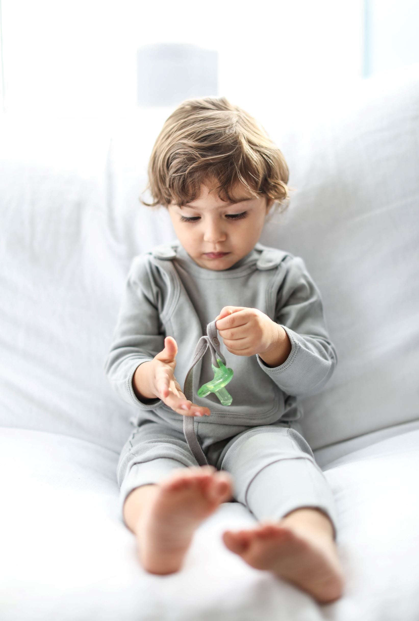 A baby is playing with the Smart Footed One-Piece + Bib - Gray by Fuchsia Milo in a living room.