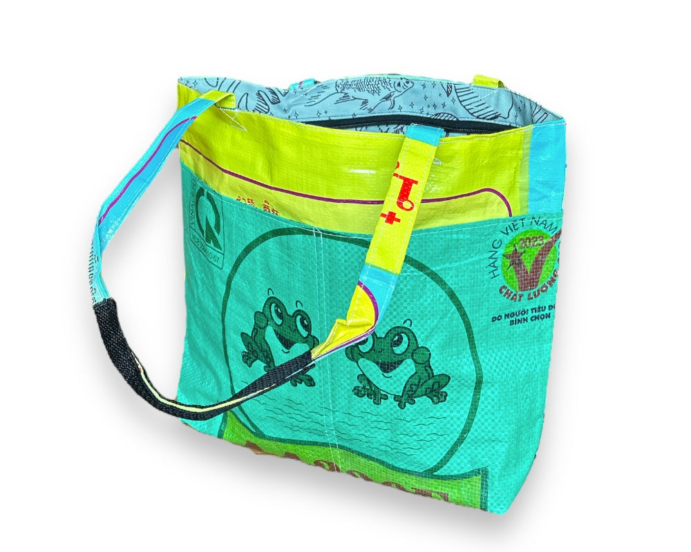 This lively Barrel Tote, made from recycled rice sacks, features whimsical frog graphics and genuine Vietnamese text, embodying a Portland-inspired design.