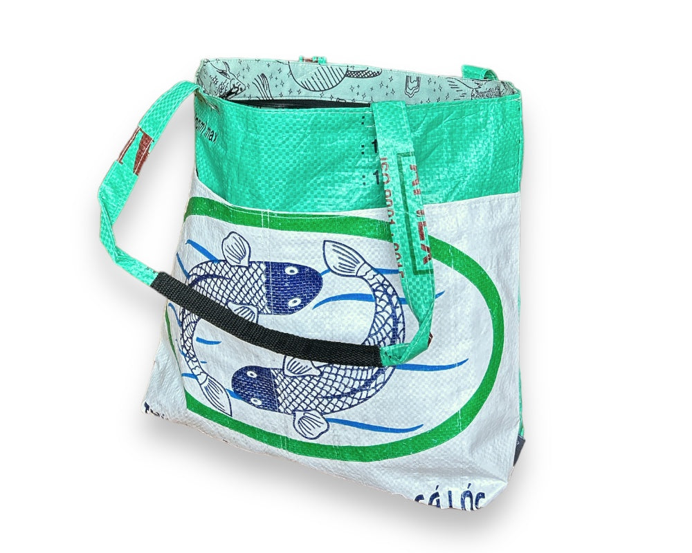 This lively Barrel Tote, made from recycled rice sacks, features whimsical frog graphics and genuine Vietnamese text, embodying a Portland-inspired design.