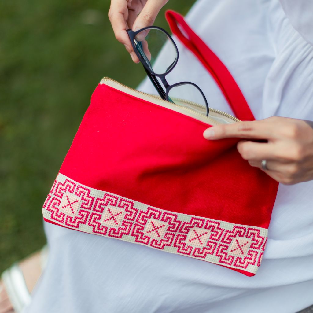 The Safa Tatreez Pouch - Red showcases exquisite Palestinian tatreez with intricate geometric patterns along the bottom edge. Hand-embroidered with care, it supports fair trade practices.