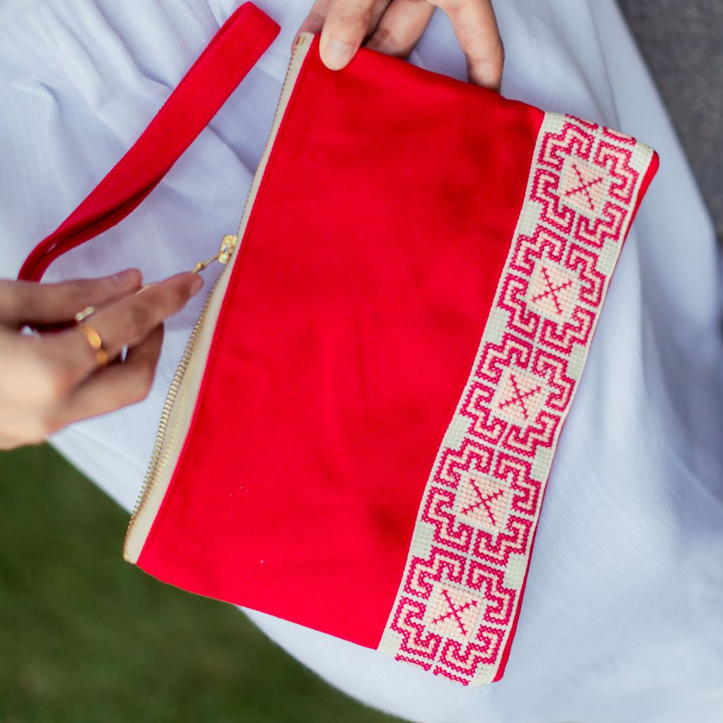 The Safa Tatreez Pouch - Red showcases exquisite Palestinian tatreez with intricate geometric patterns along the bottom edge. Hand-embroidered with care, it supports fair trade practices.