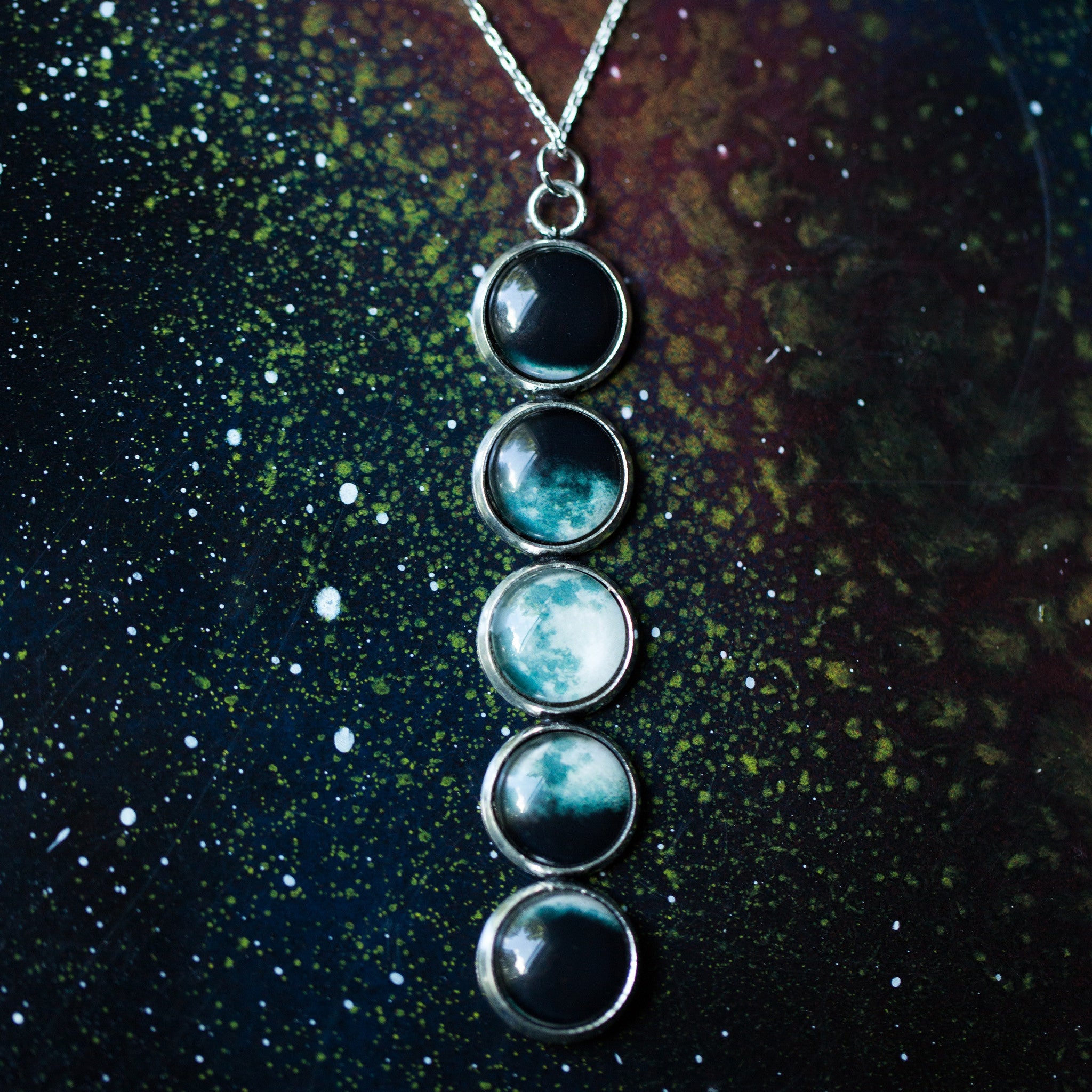 Introducing the Moon Phase Pendant Necklace: a breathtaking piece adorned with five round pendants, each beautifully depicting the phases of the moon against a starry background, capturing the splendor of the lunar cycle.